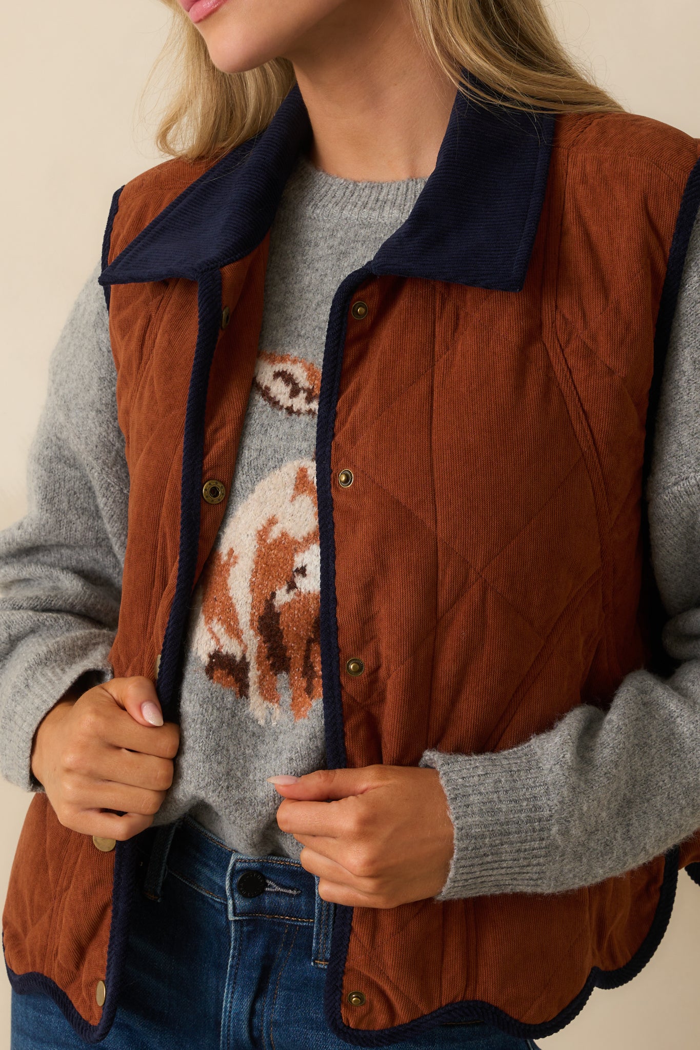 Detailed view of diamond stitching, scalloped hem, and navy trim on the ginger brown vest