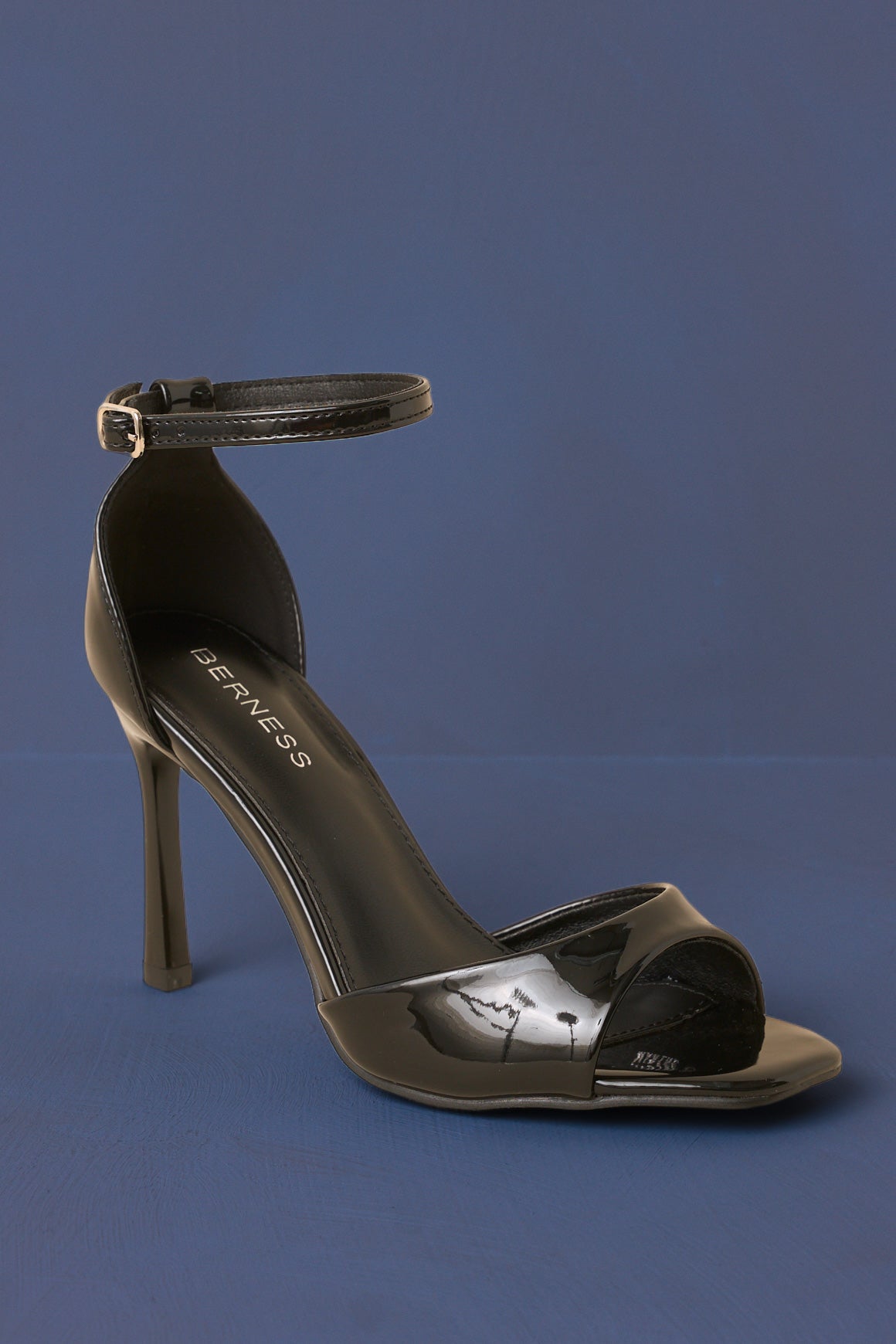 Black, ankle strap, open toed stilettos in front of a blue backdrop.  