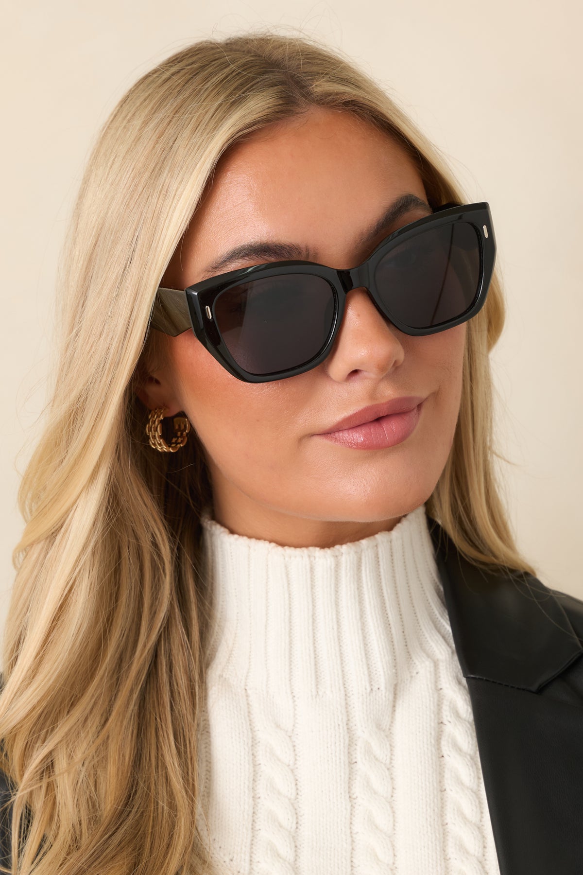 Glossy black sunglasses feature a bold square frame, dark lenses, gently lifted outer corners, and wide arms with gold-tone accents.