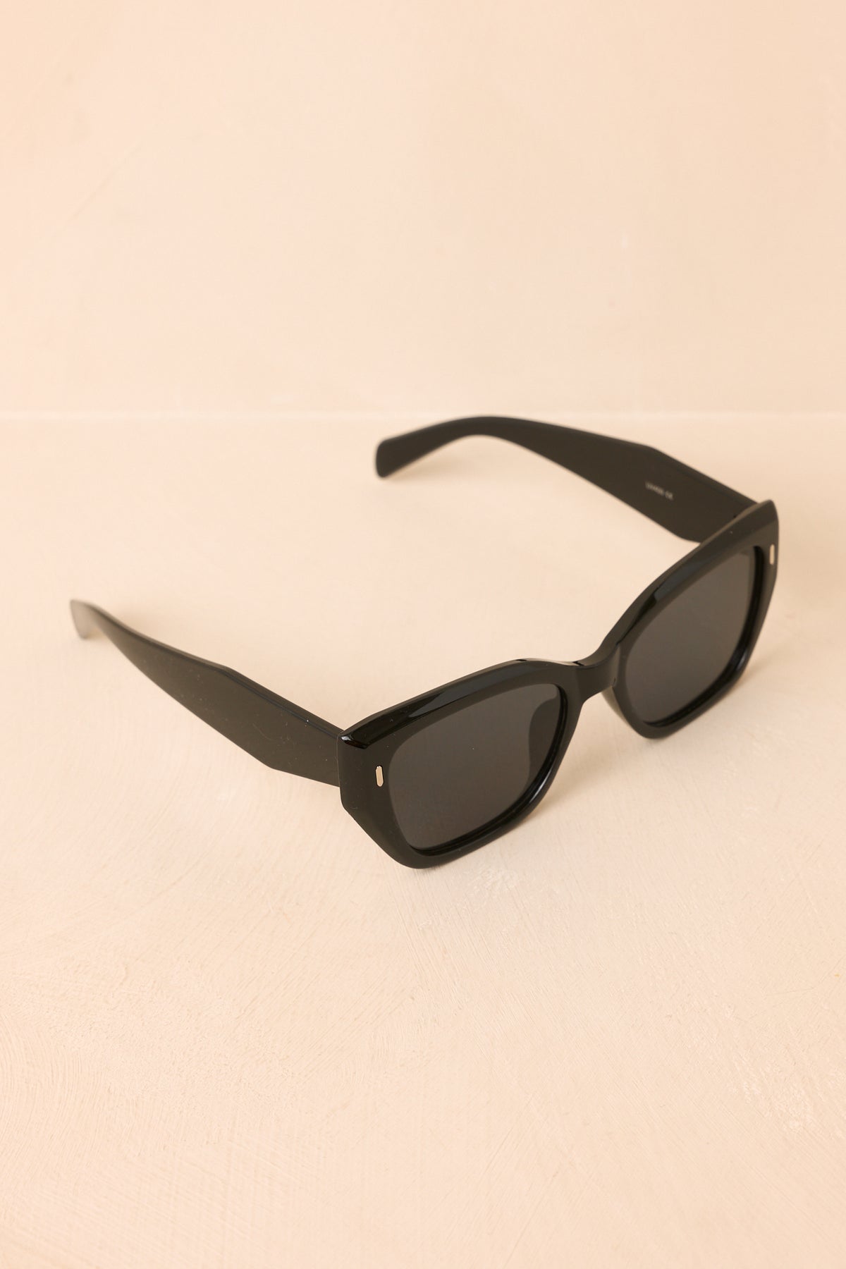 Front view of black sunglasses showcases the bold square frames, dark tinted lenses, and gently raised outer corners.