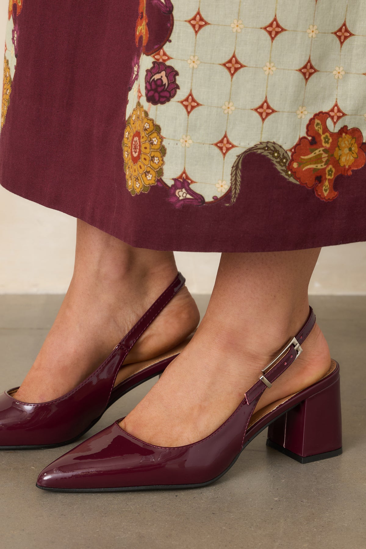 Glossy wine red heels feature a sleek pointed toe and slingback design with an adjustable strap.