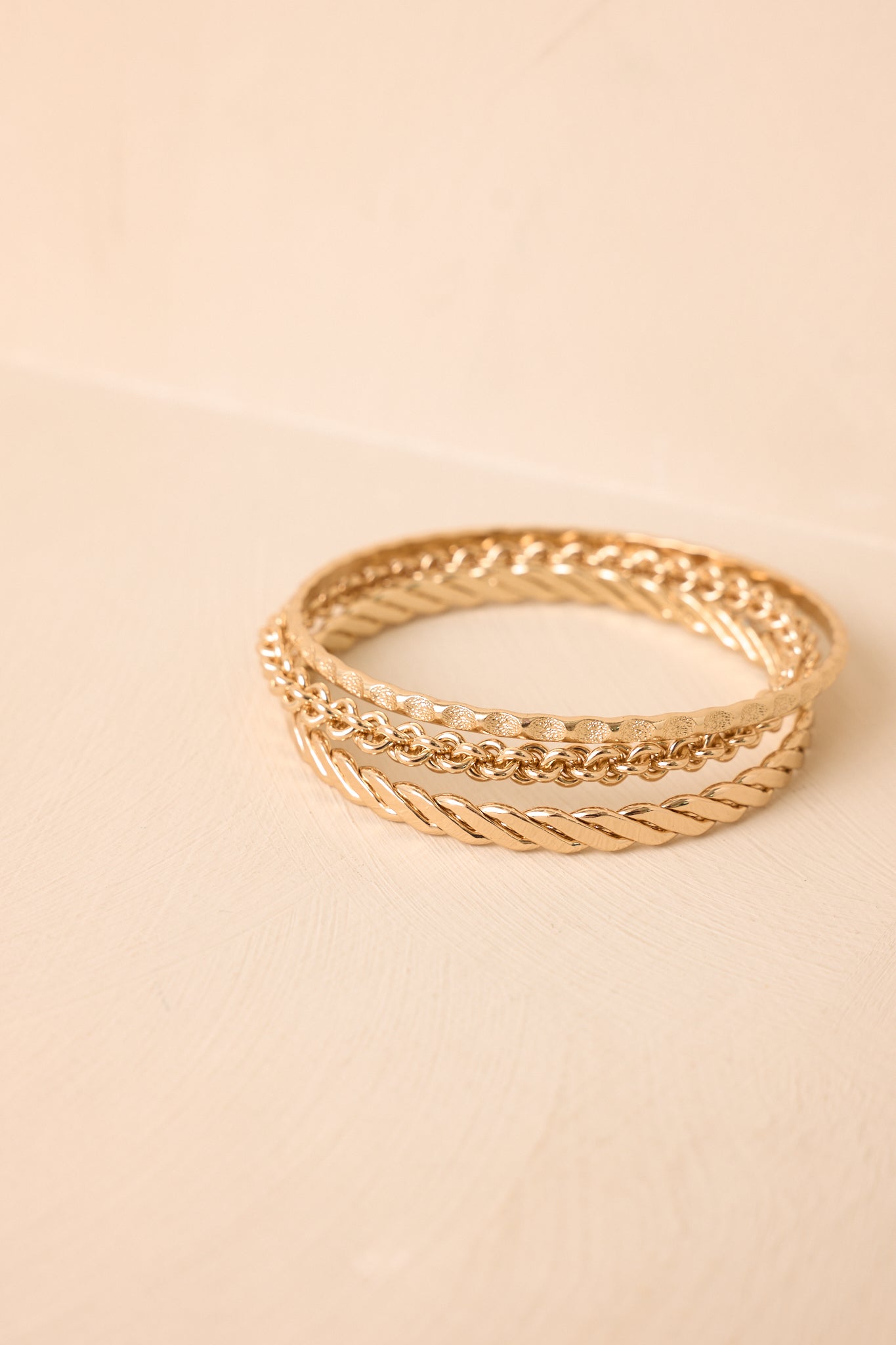 Gold bangle set featuring layered textures and complementary designs presented on a beige backdrop.