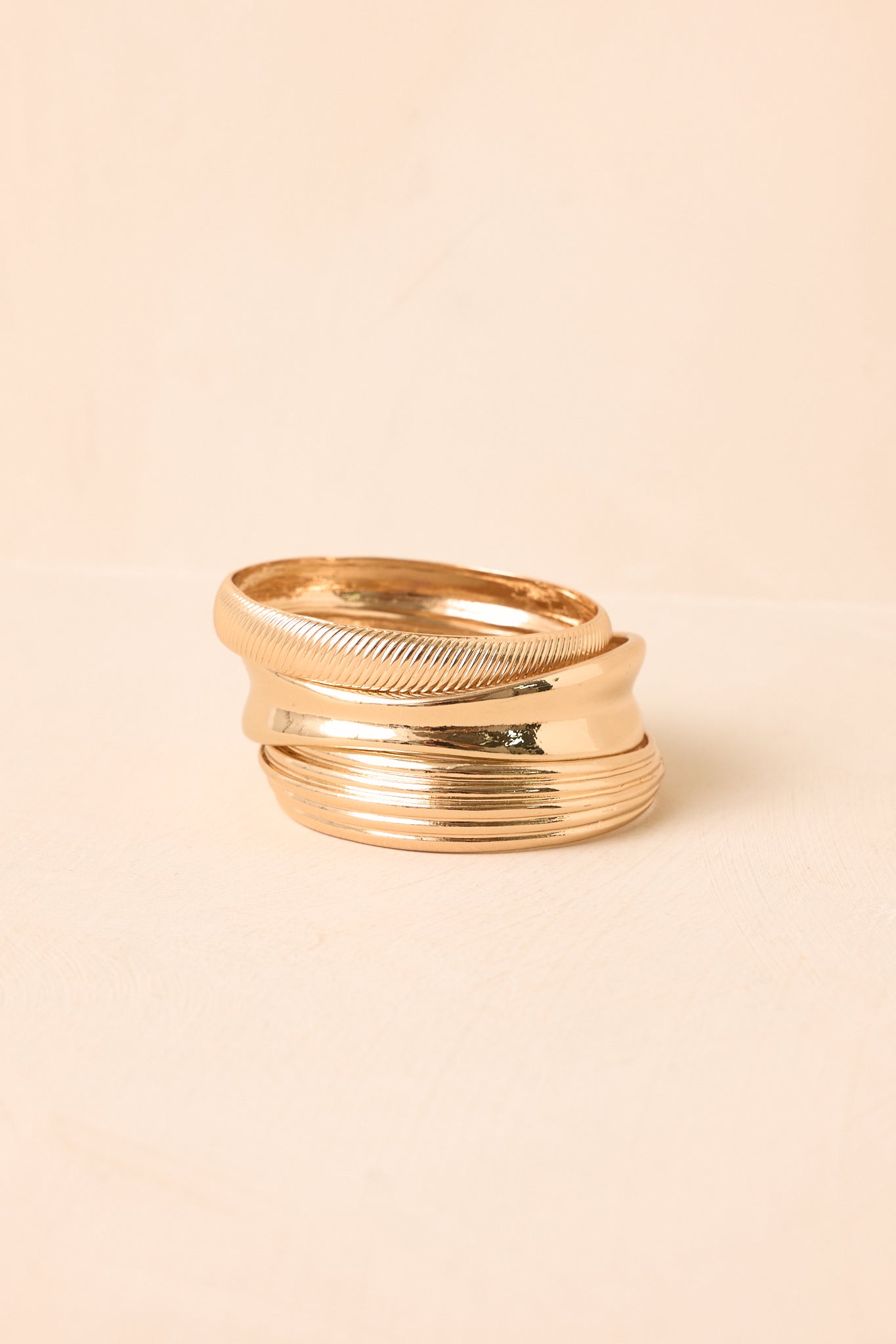 Gold bracelet set showcasing three distinct bangle styles, including a wide polished design and ridged detailing.