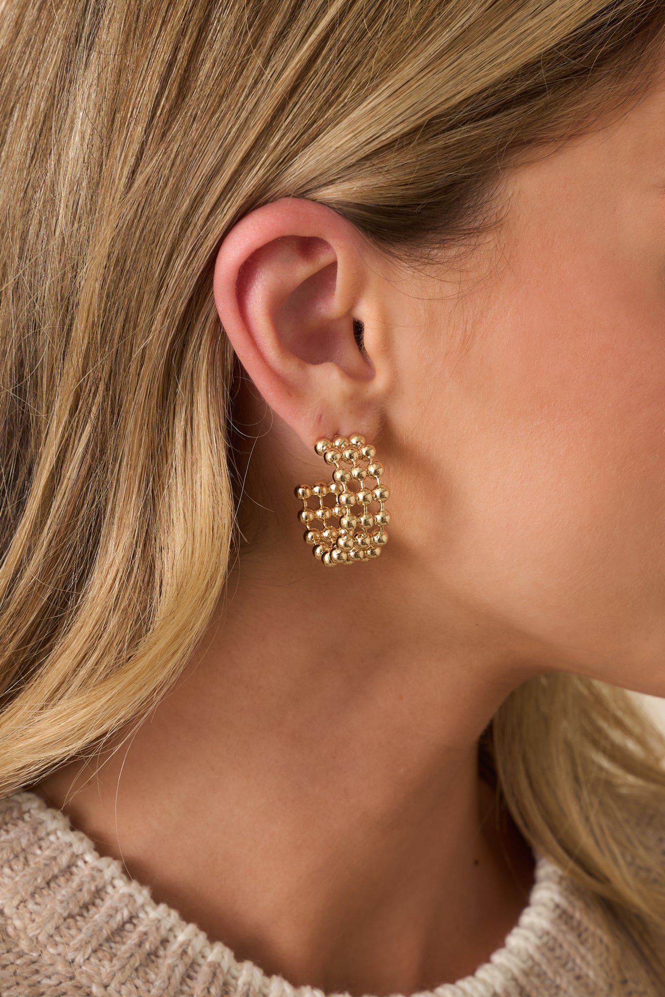 A close-up of one earring showing the detailed gold beads, open hoop structure, and secure post backing.