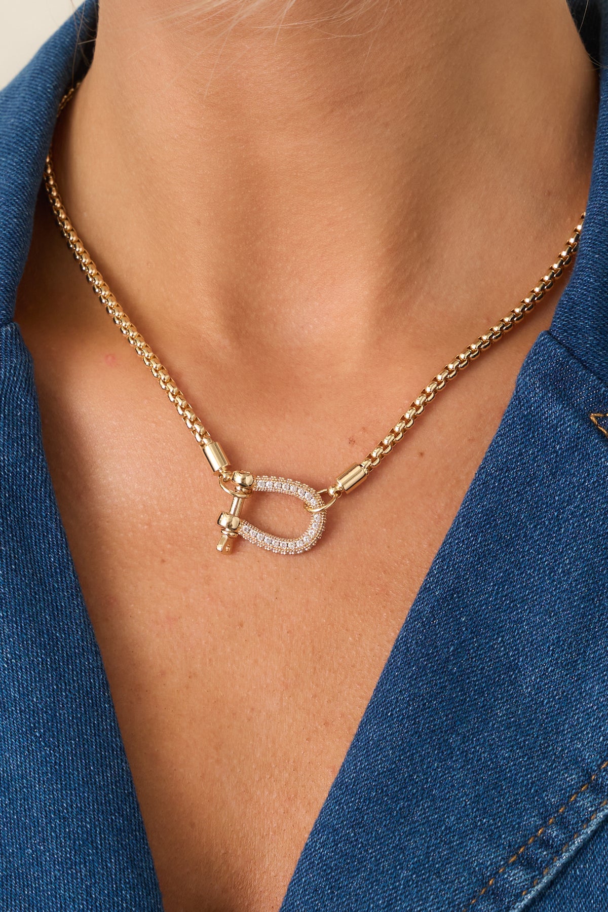 Gold-tone box chain necklace displayed against a beige background, highlighting the structured chain and sparkling decorative clasp.