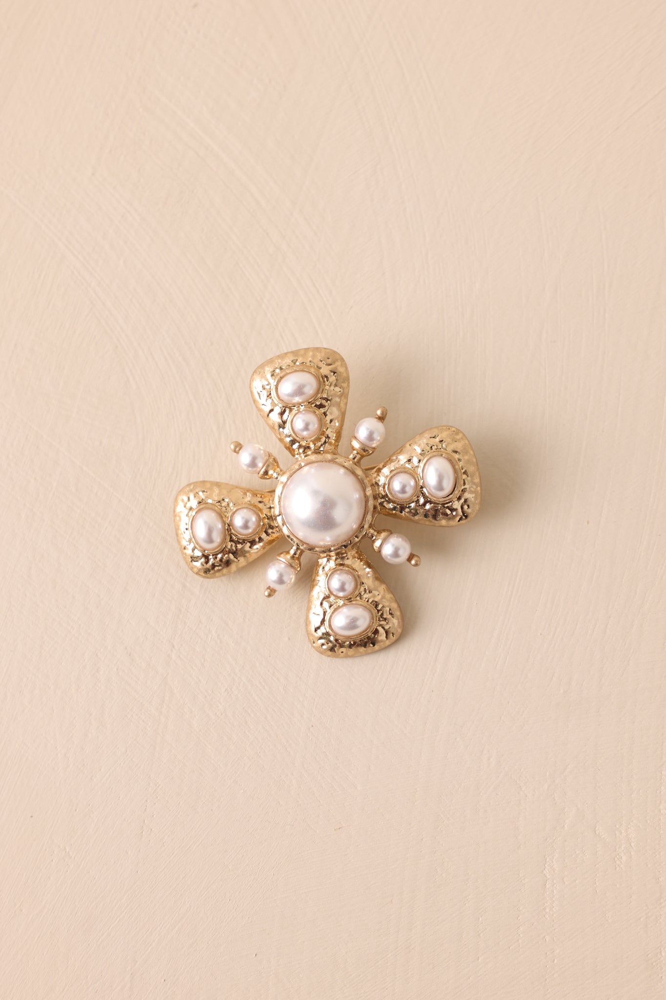 Close view of the gold brooch highlighting the large faux pearl centerpiece and surrounding triangular sections with pearl accents.