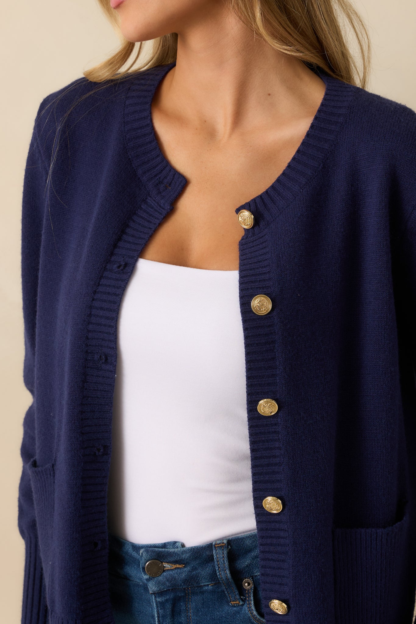 Detailed look at the gold button closure, patch pockets, and navy knit texture of the cardigan.