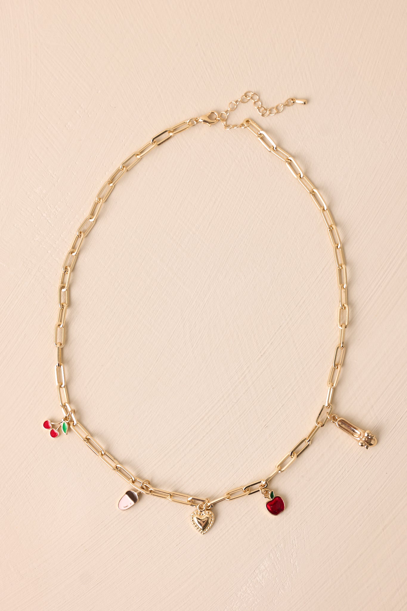 Gold charm necklace with a rectangular chain featuring a red apple, heart, ballet shoe, acorn, and cherry charms shown from the front.