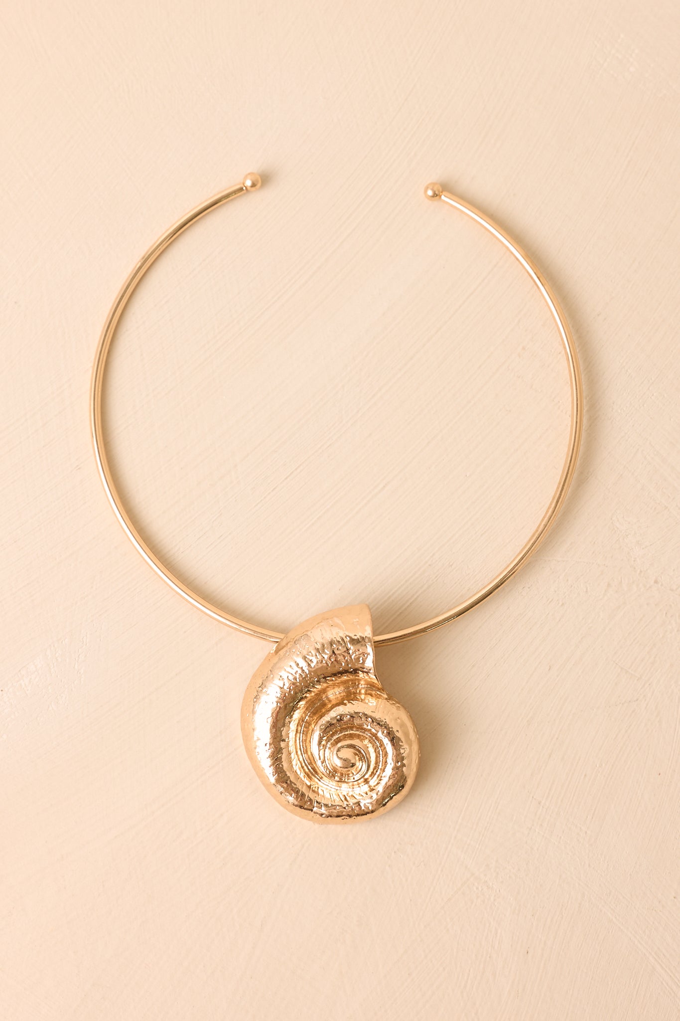 Gold collar necklace displayed against a beige background highlighting the dimensional shell-inspired centerpiece.