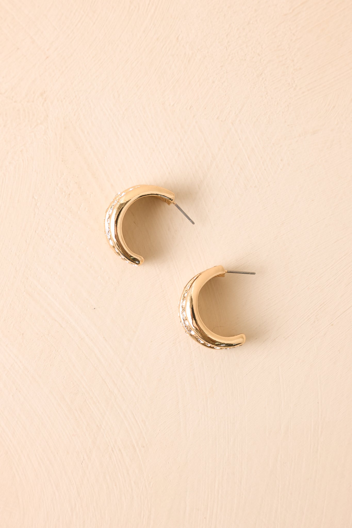 Gold crystal hoop earrings displayed against a beige background, highlighting their radiant shine and elegant shape.
