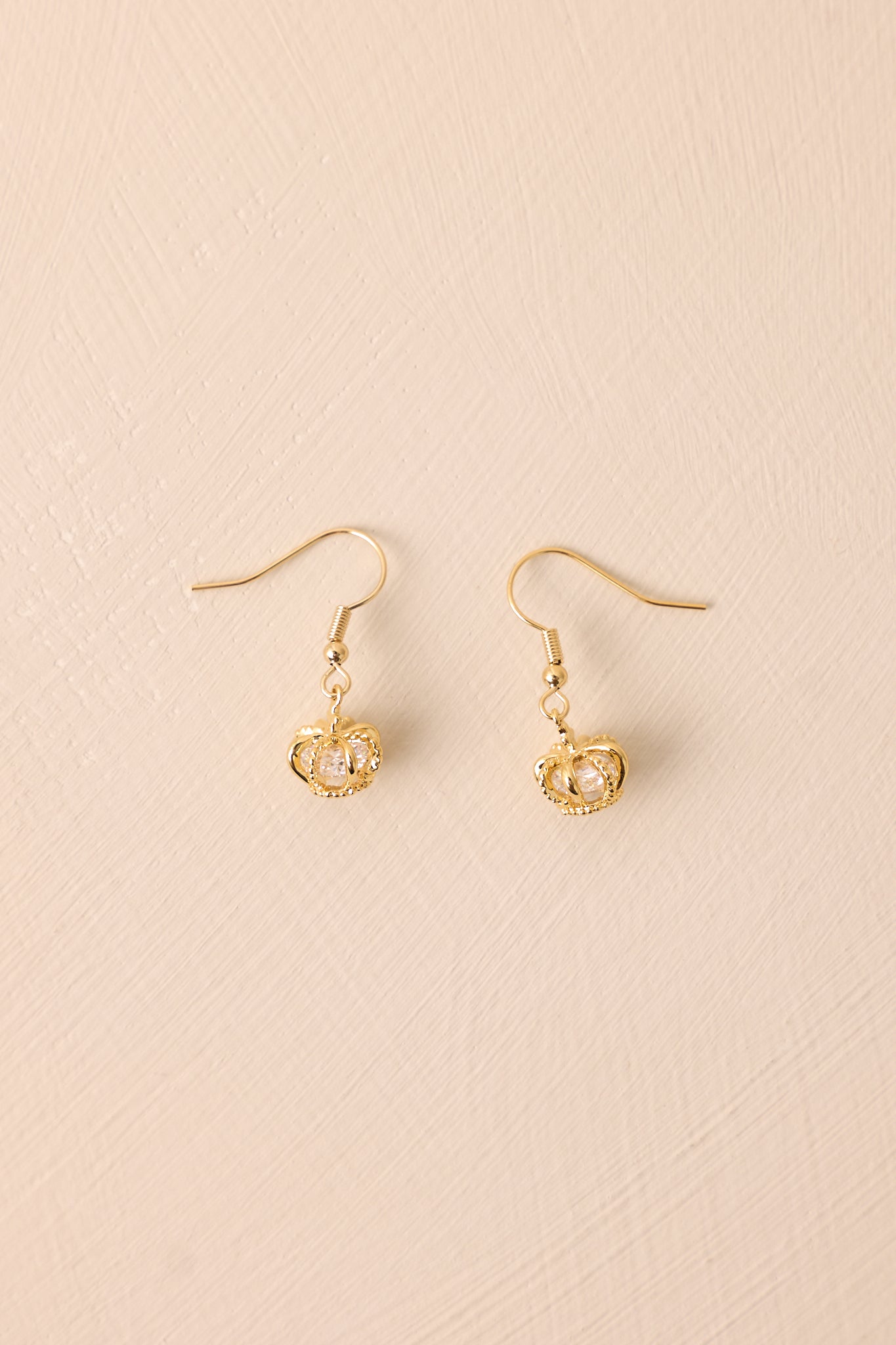 The gold dangle earrings displayed against a neutral beige background, showcasing their elegant design and intricate details.