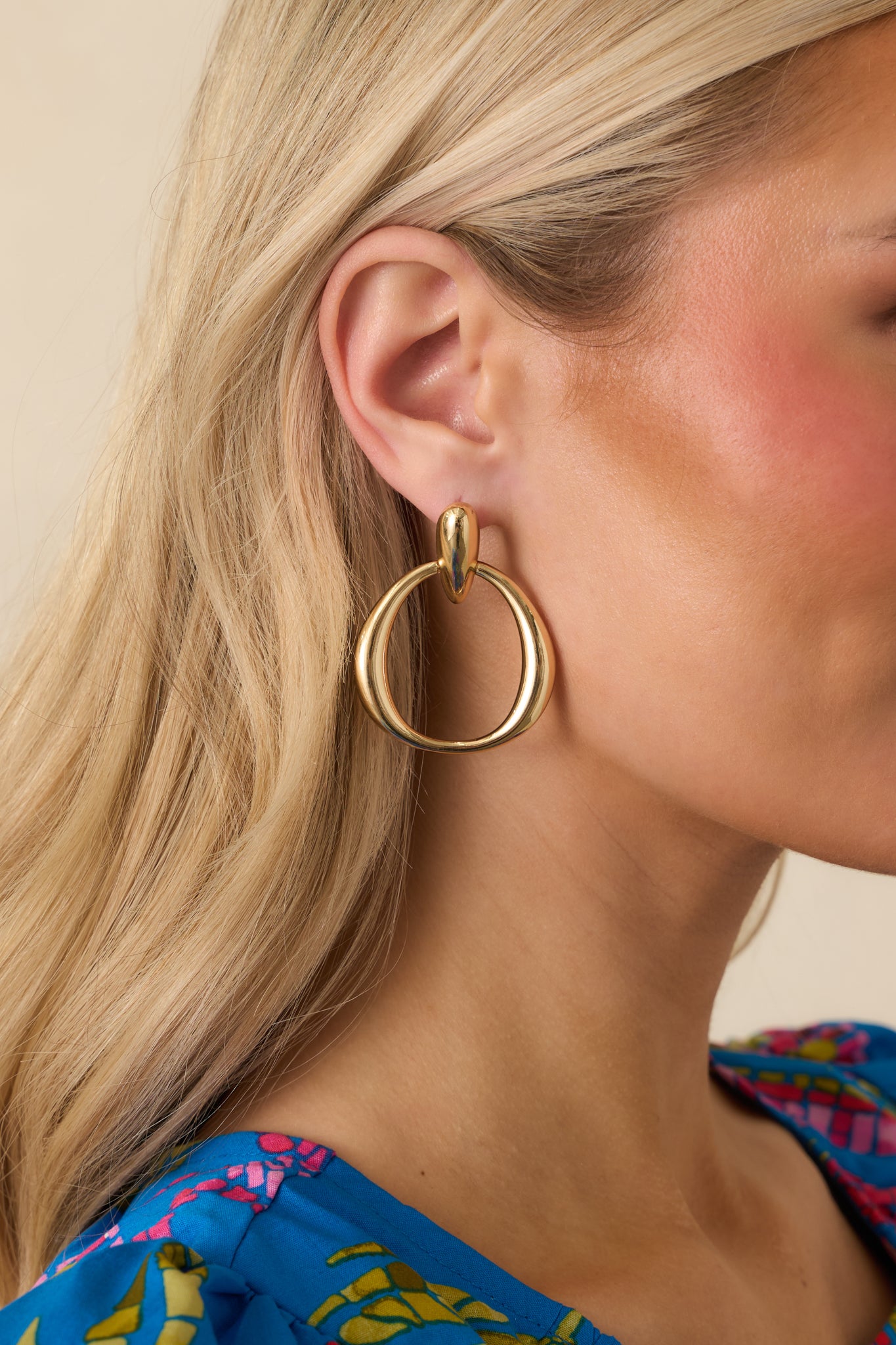Cropped view of gold earrings highlighting teardrop-shaped stud and circular drop link.
