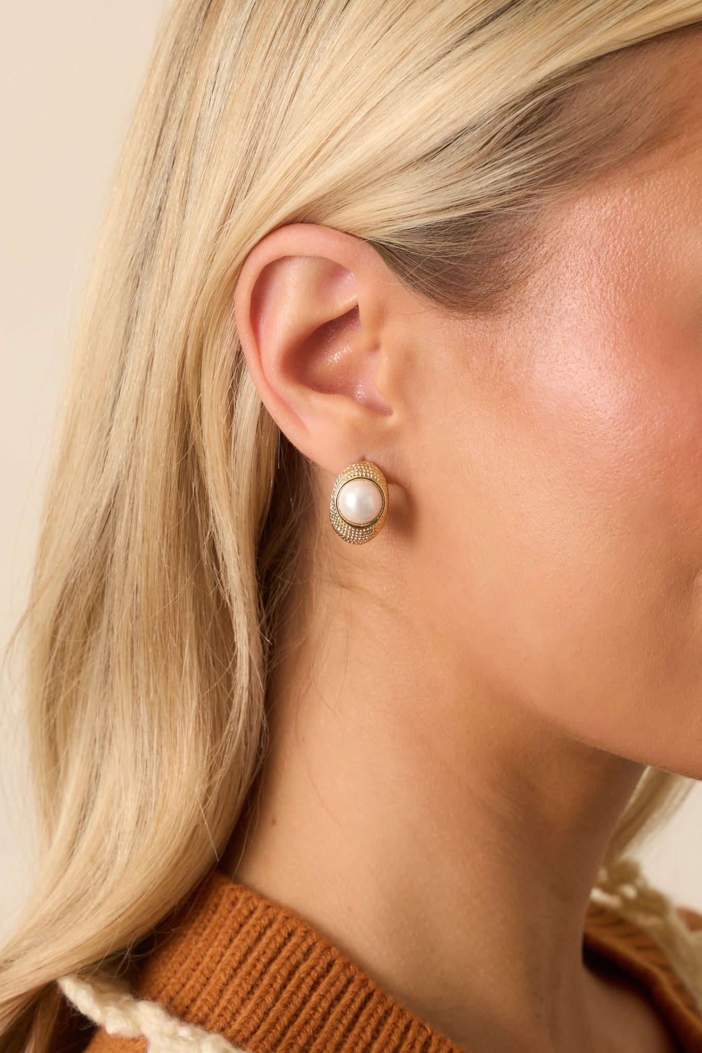 A cropped view of the gold earrings showing a textured oval frame with center ivory faux pearl.