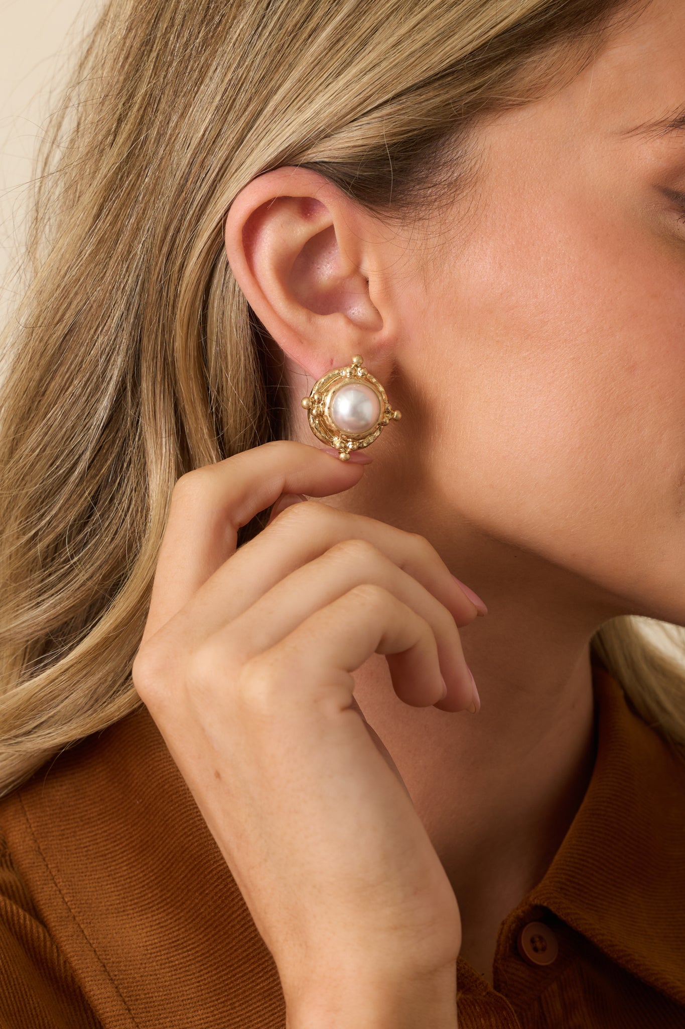 Gold earrings with textured round frame and raised ivory faux pearl center.