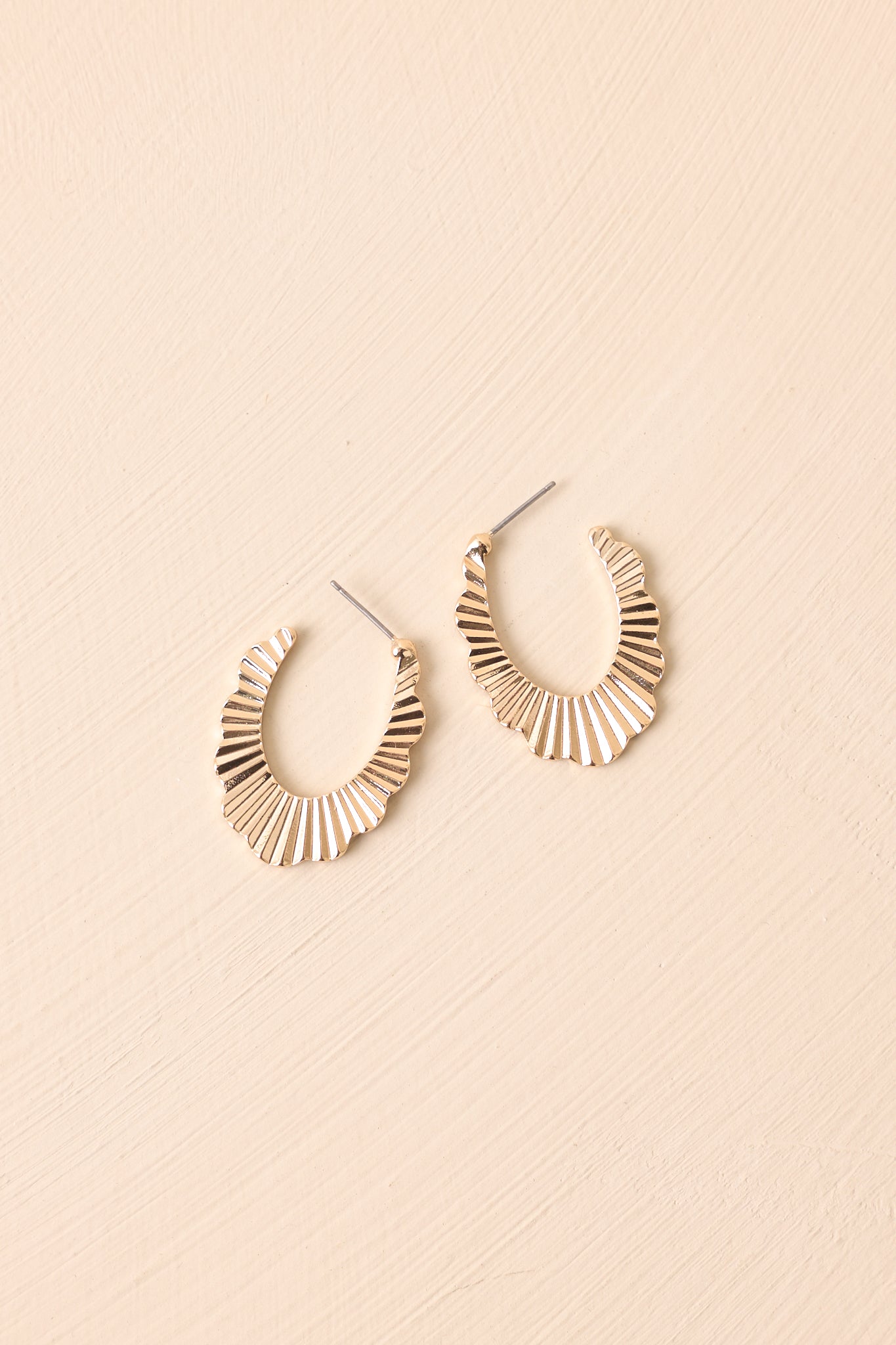 A close view of the gold earrings with scalloped edges, an incomplete hoop design, and lined texture.