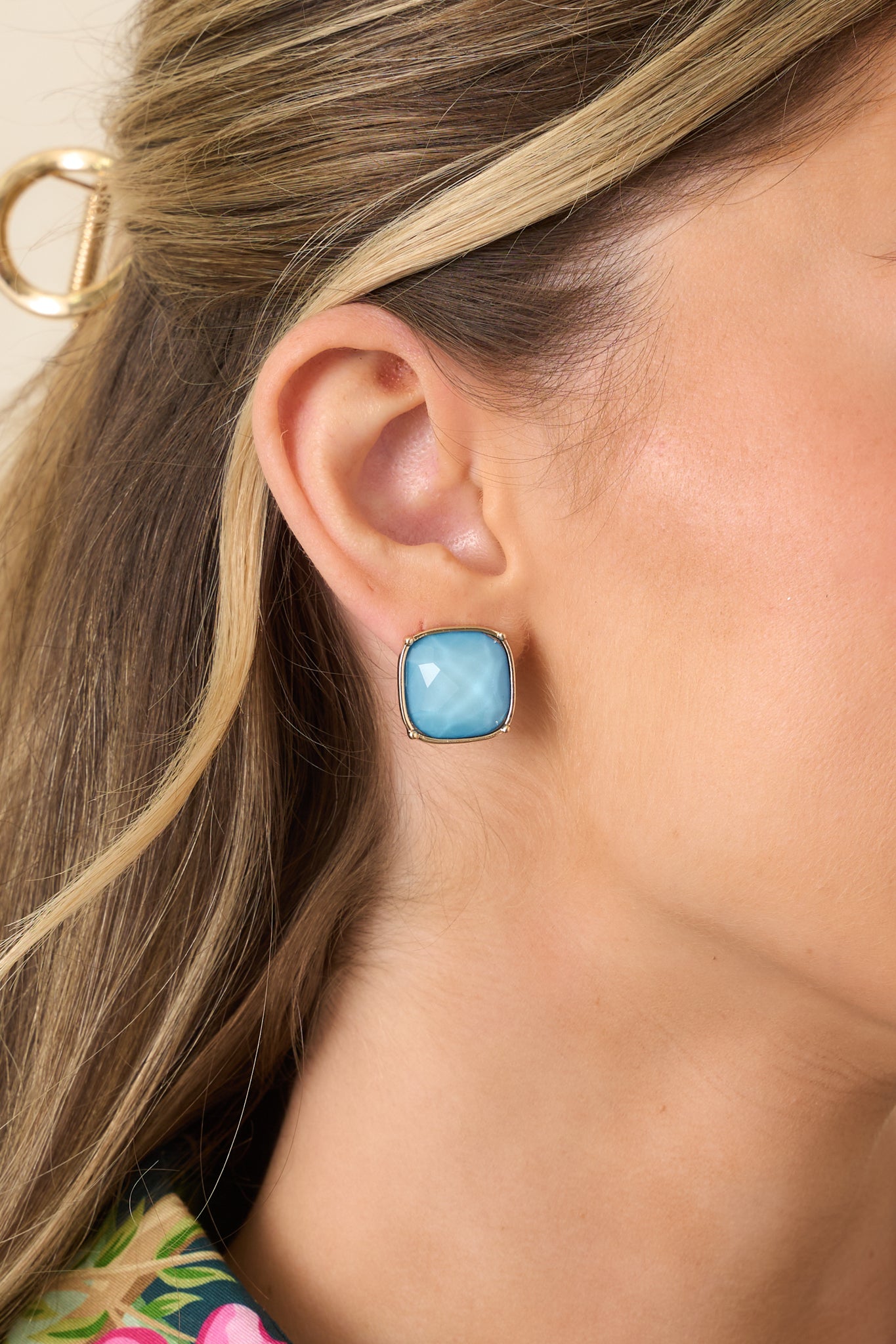Close-up of a gold-tone stud earring highlighting the faceted light blue stone and smooth polished metal frame.