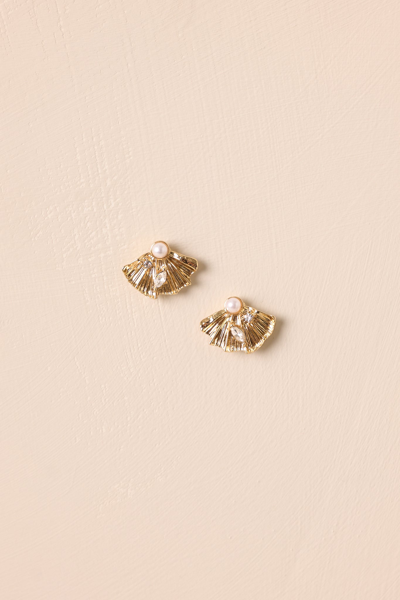Gold fan stud earrings displayed on a beige background, showcasing the faux pearl top and rhinestone detailing.