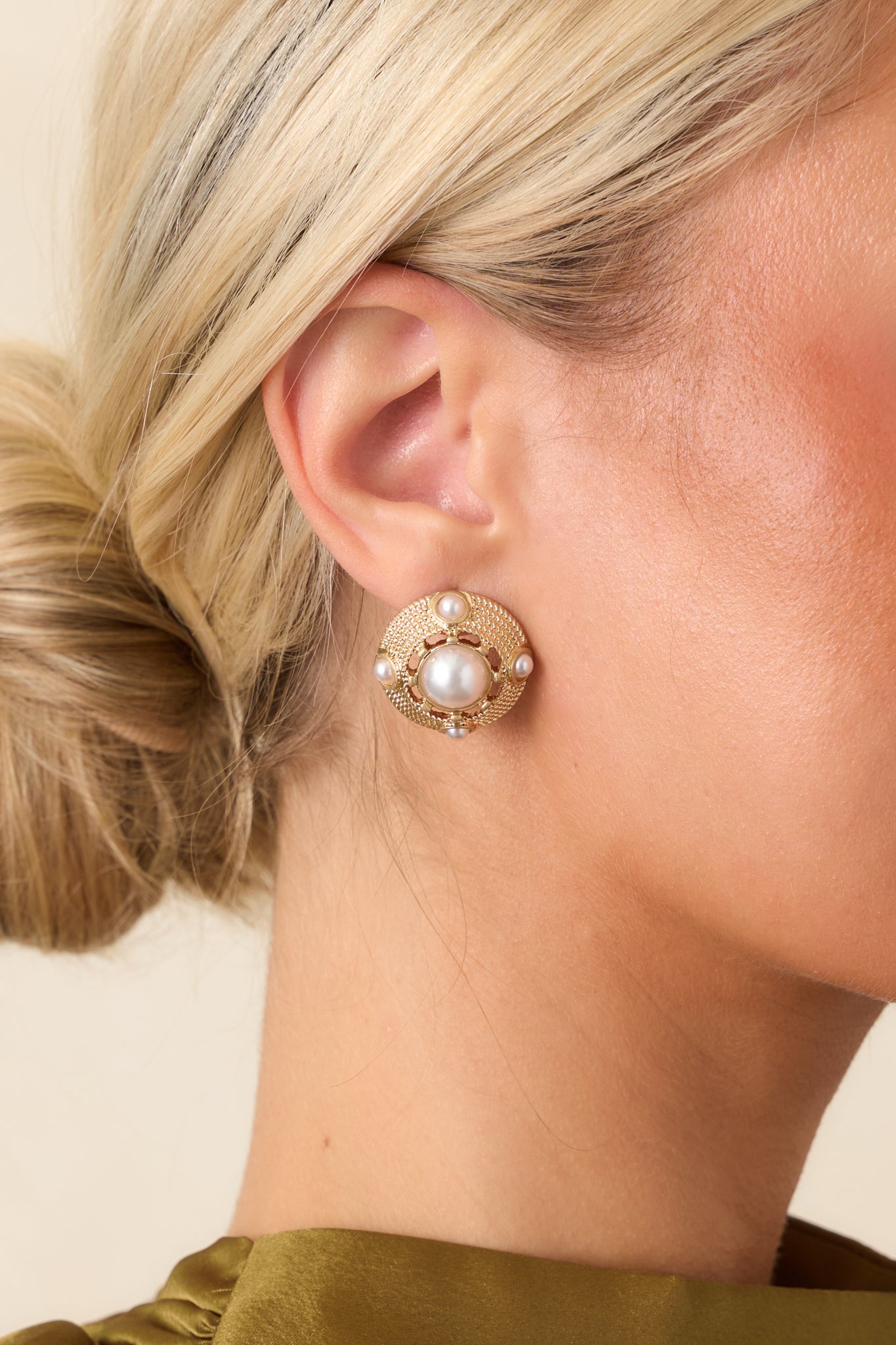 Close-up of a gold-tone circular earring highlighting the textured setting, prominent faux pearl center, and surrounding smaller pearl accents.