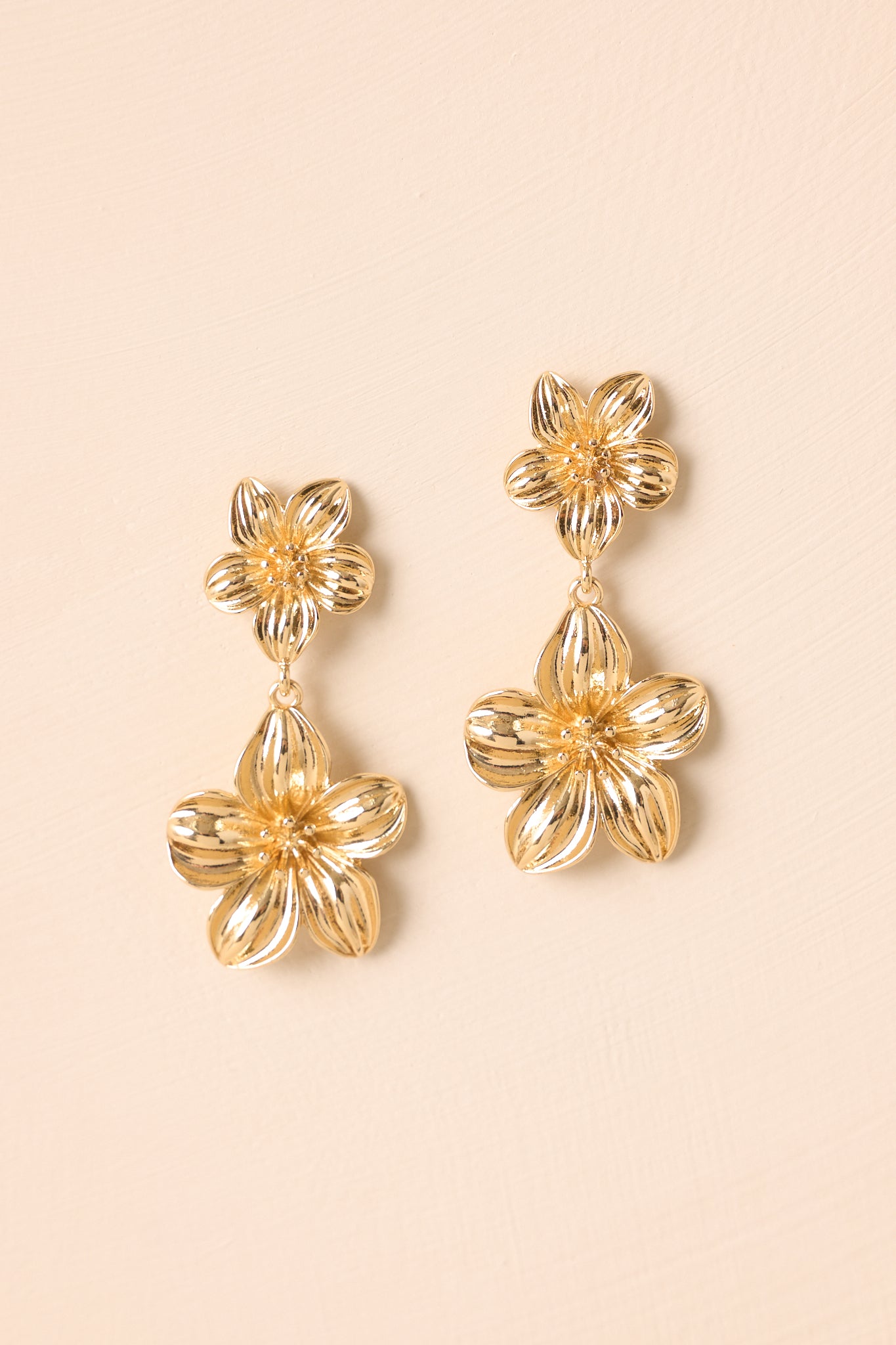 Gold flower earrings displayed against a beige background featuring a sculptural floral drop design.