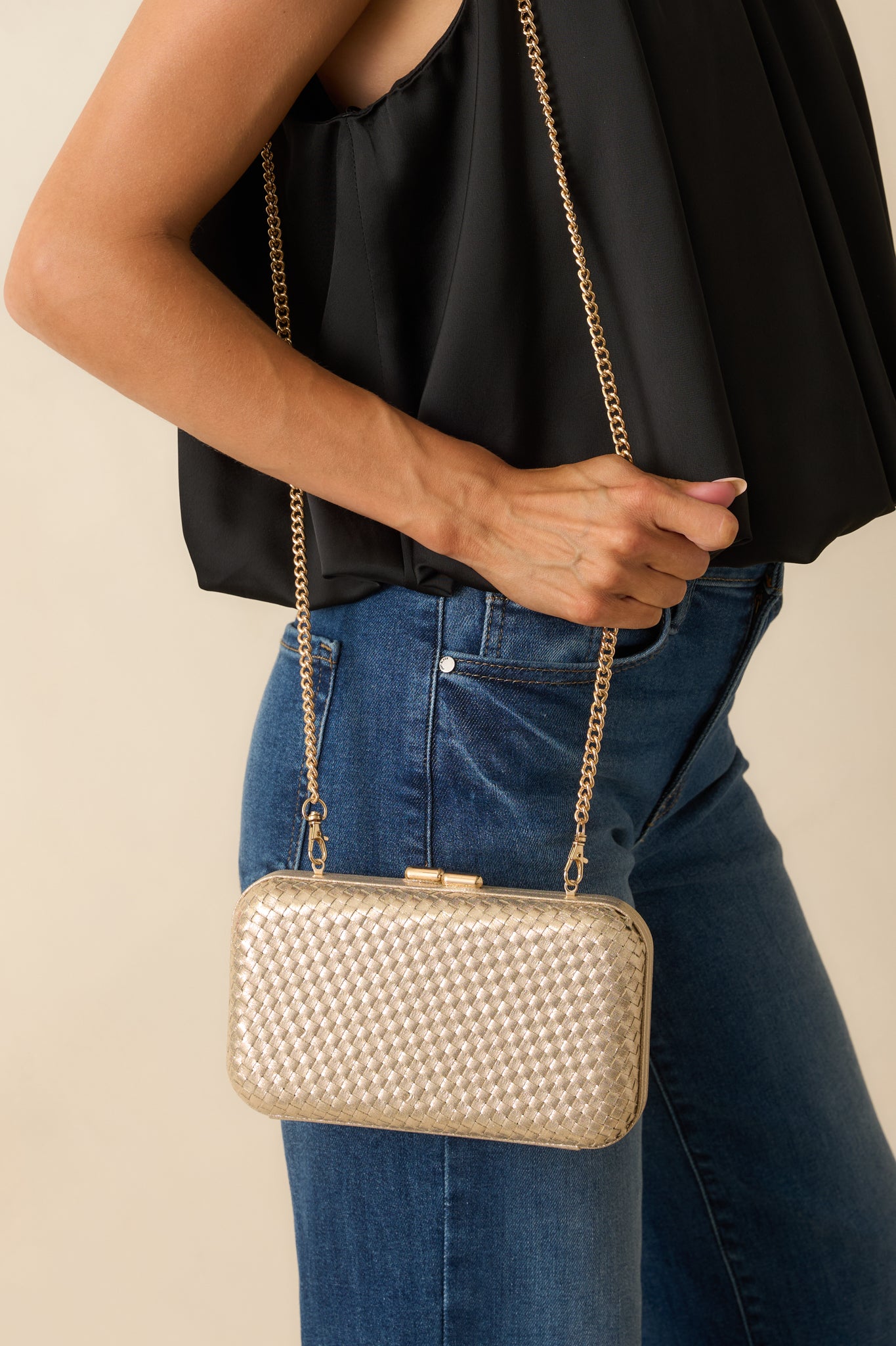 Gold hard case clutch displayed with its optional chain crossbody strap and rounded edges visible.