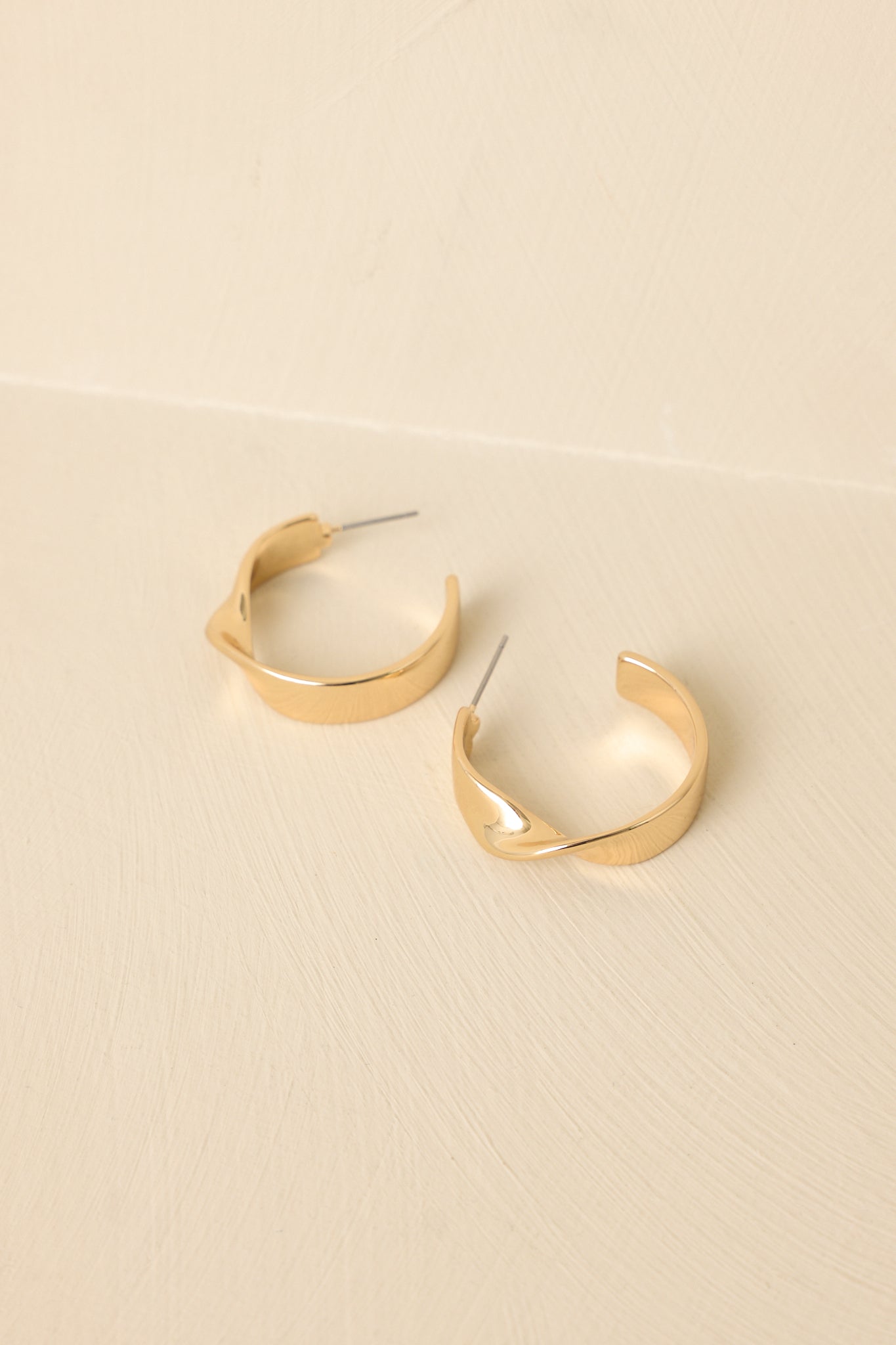 Close-up of gold hoop earrings highlighting the twisted front detail, smooth flat band, and post backing.