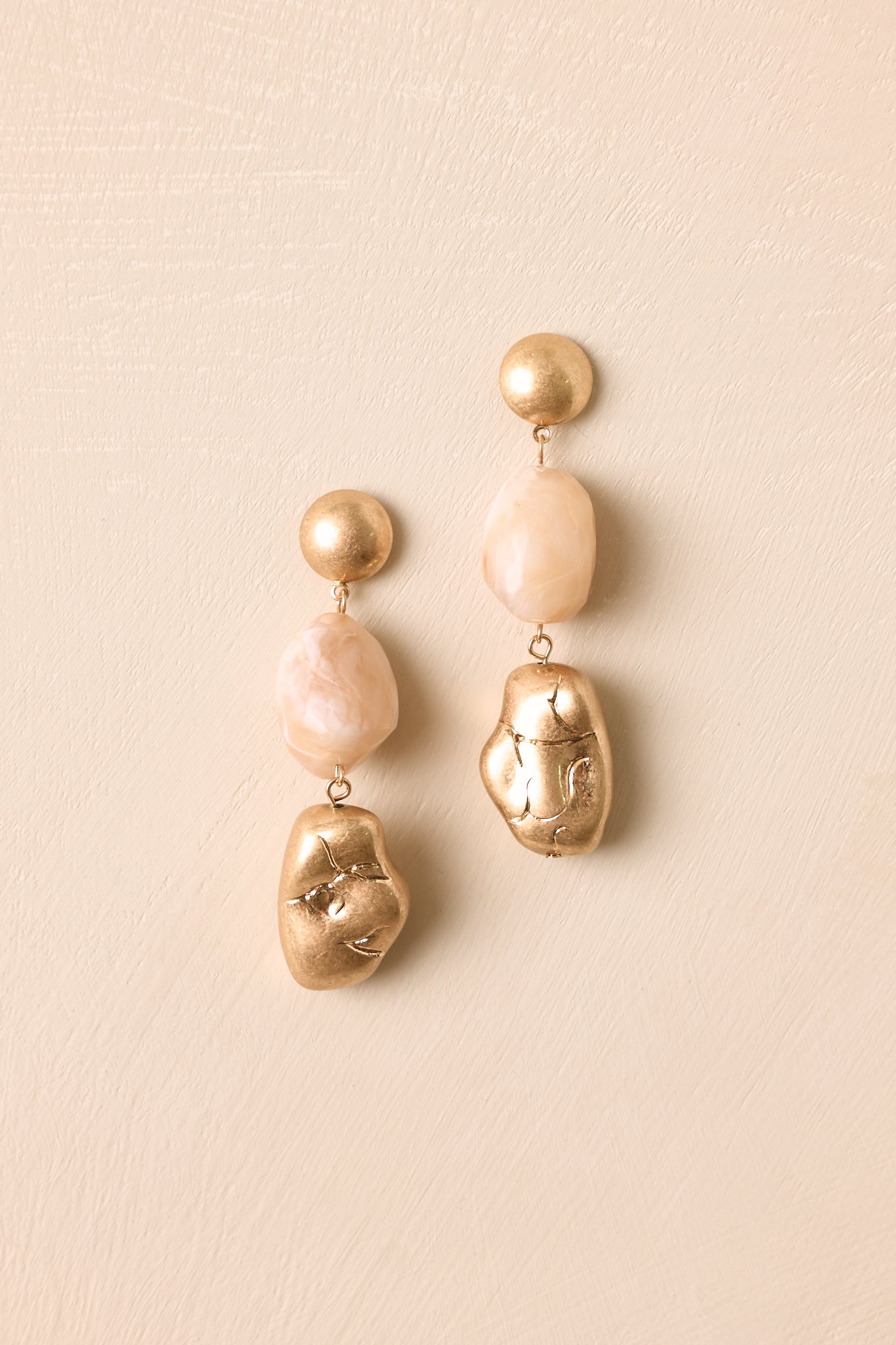 Gold and ivory resin earrings displayed against a beige background, highlighting the brushed finish and dimensional shape.