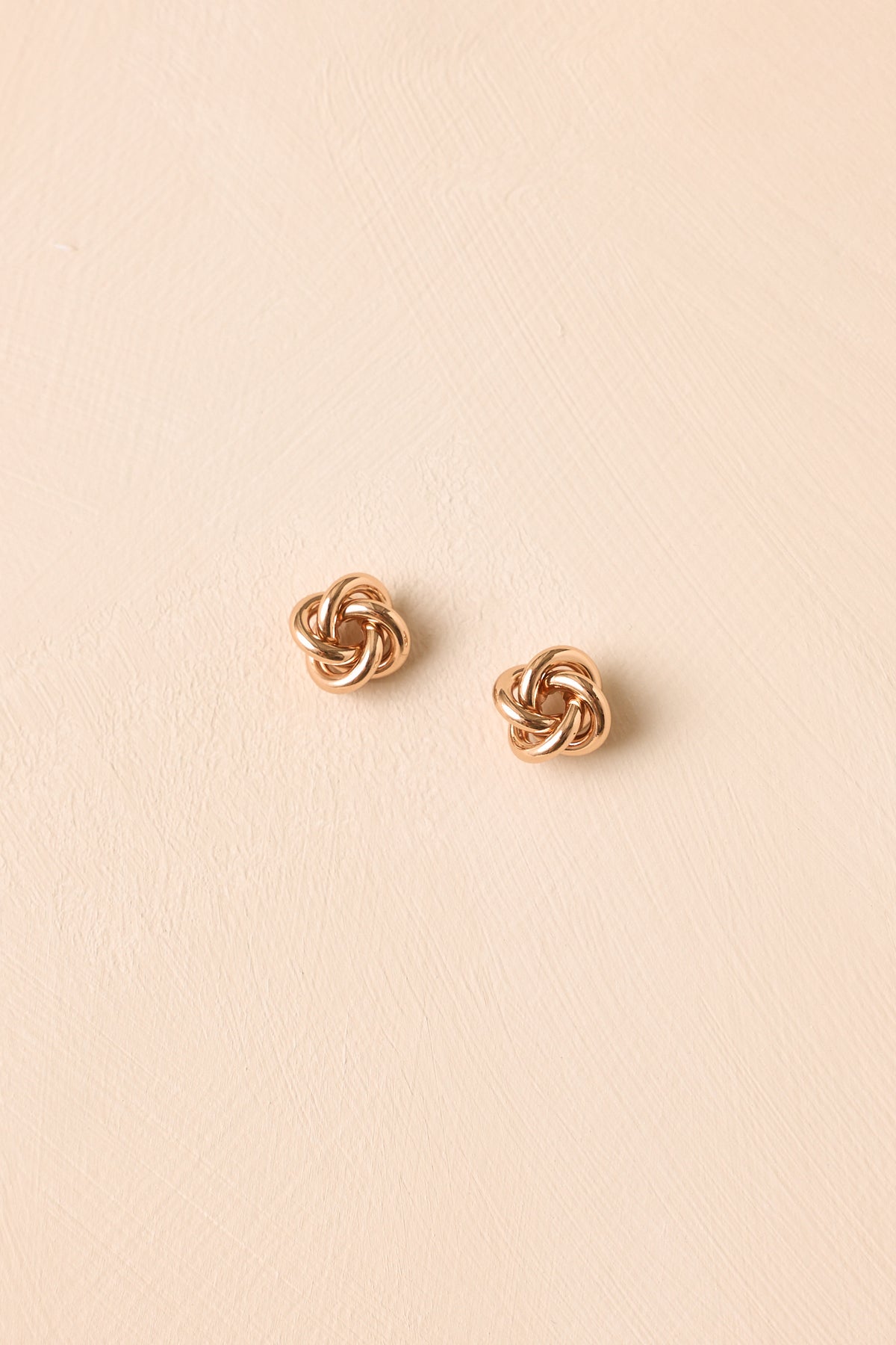 Gold knot stud earrings displayed against a neutral background, featuring a classic rounded shape and reflective polished finish.