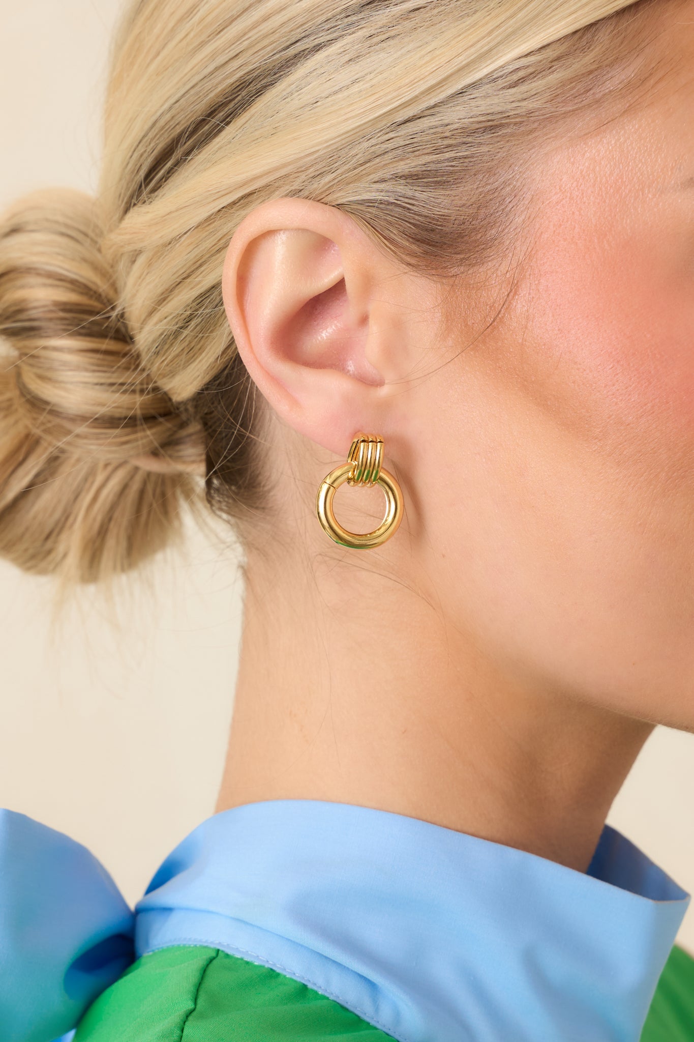 Close-up view of gold layered earrings emphasizing the polished round drop and textured stacked elements at the stud.