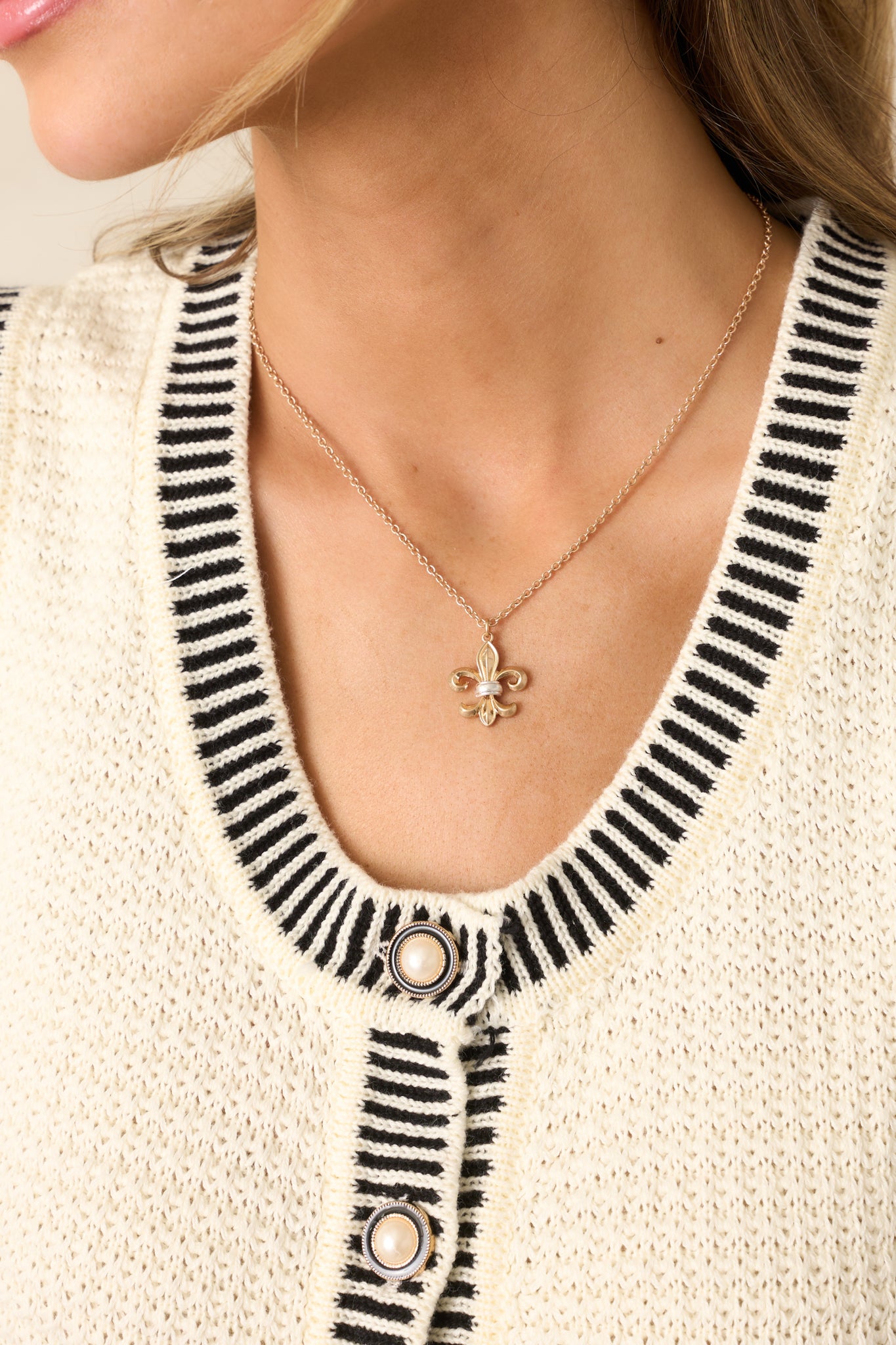 A gold necklace featuring a delicate gold chain with a classic gold fleur-de-lis pendant.