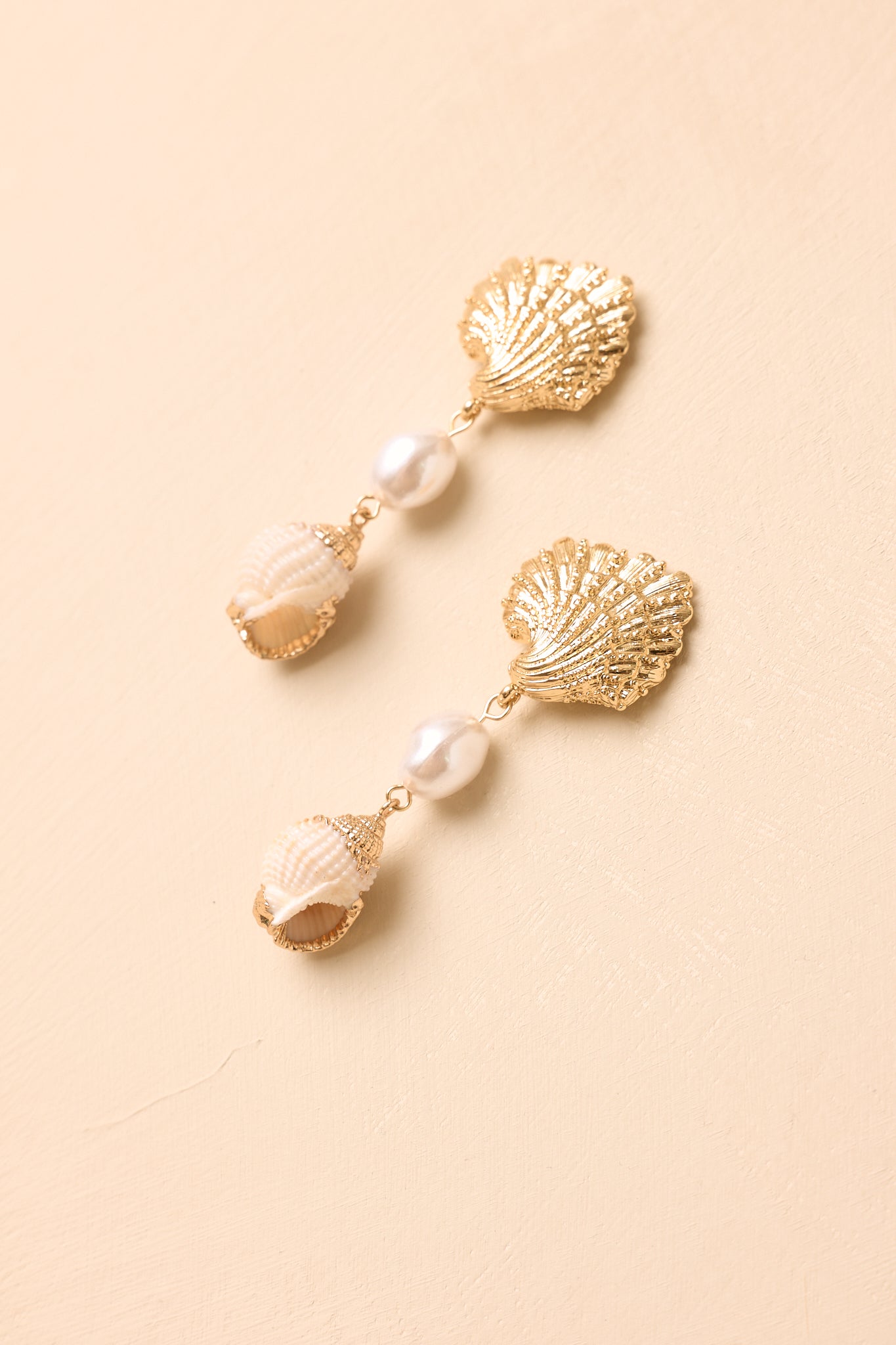 Gold and pearl earrings displayed against a beige background, highlighting the textured finish and elegant design.