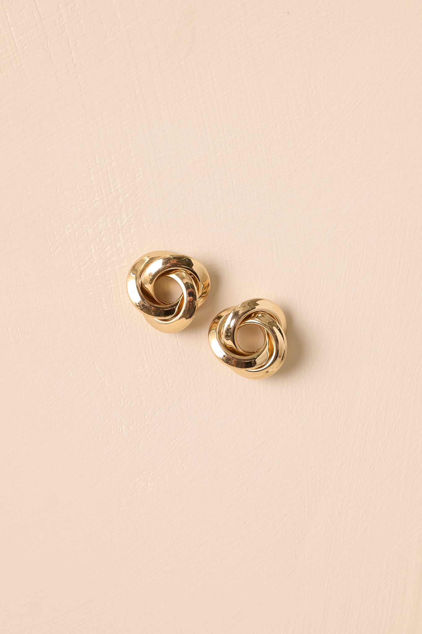 Gold twisted spiral earrings displayed against a beige background, emphasizing the hollow center and elegant shape.