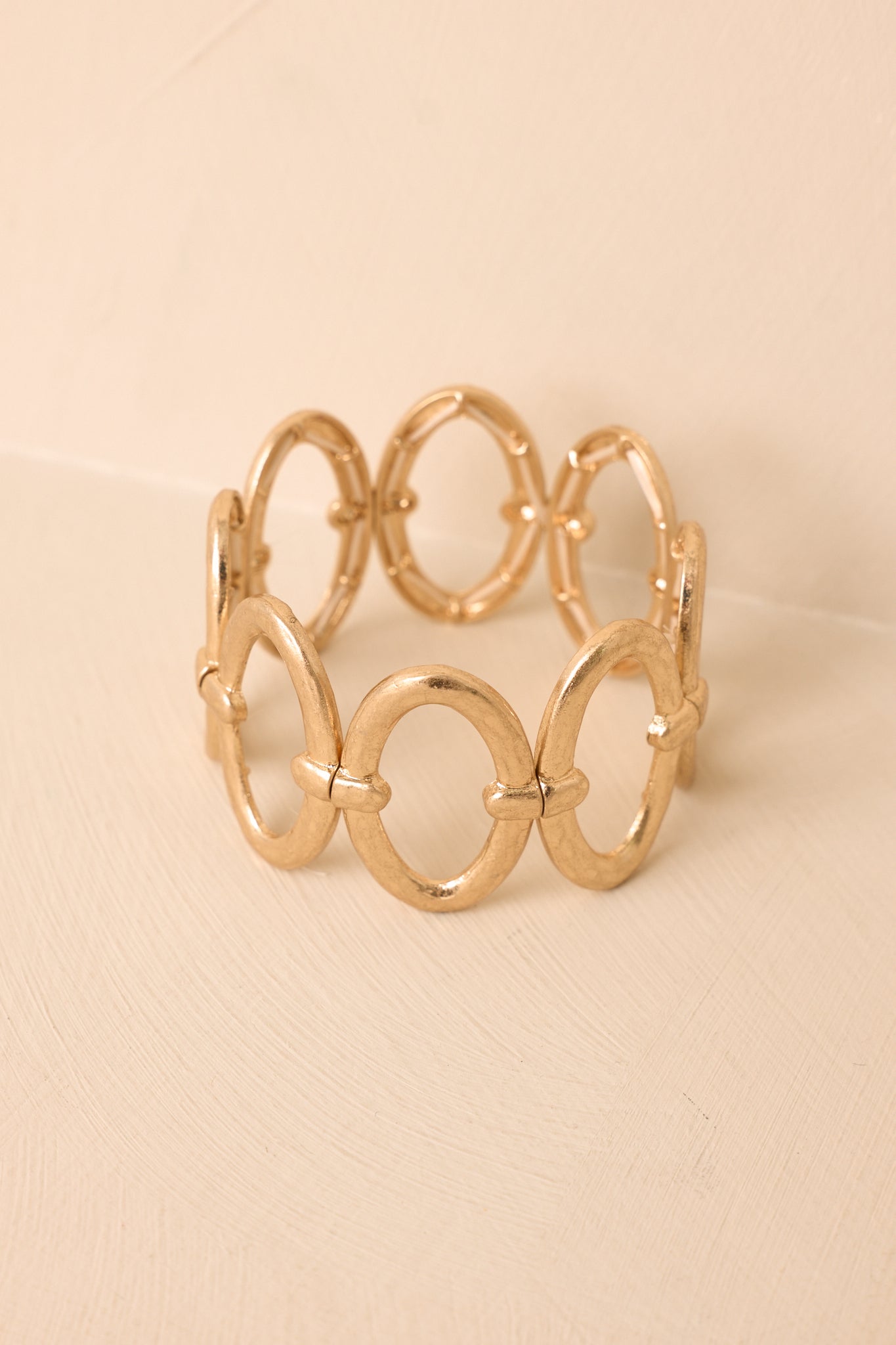 Gold statement bracelet showcasing oversized metallic links and a flexible stretch construction against a beige background.