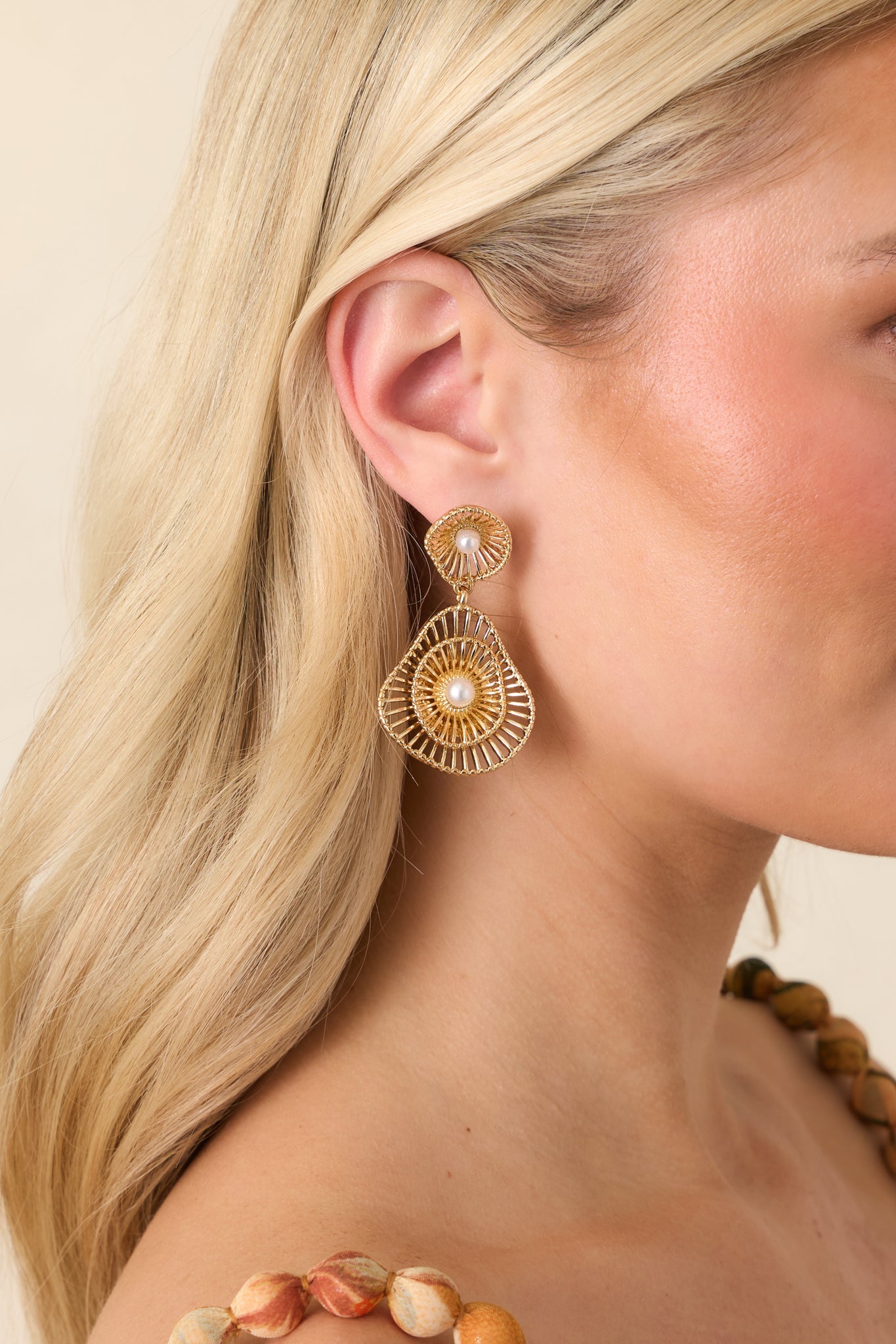 Cropped view of gold statement earrings featuring sunburst-inspired detailing and pearl accents.
