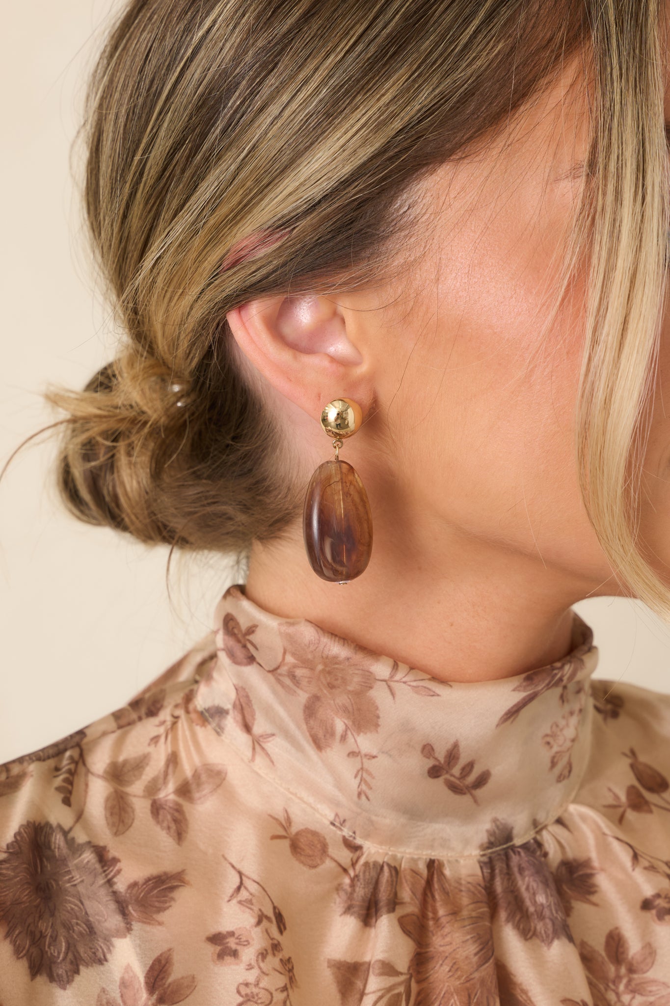 Close view of the earrings highlighting the polished gold-tone studs, smooth tortoise beads, and elongated oval silhouette.