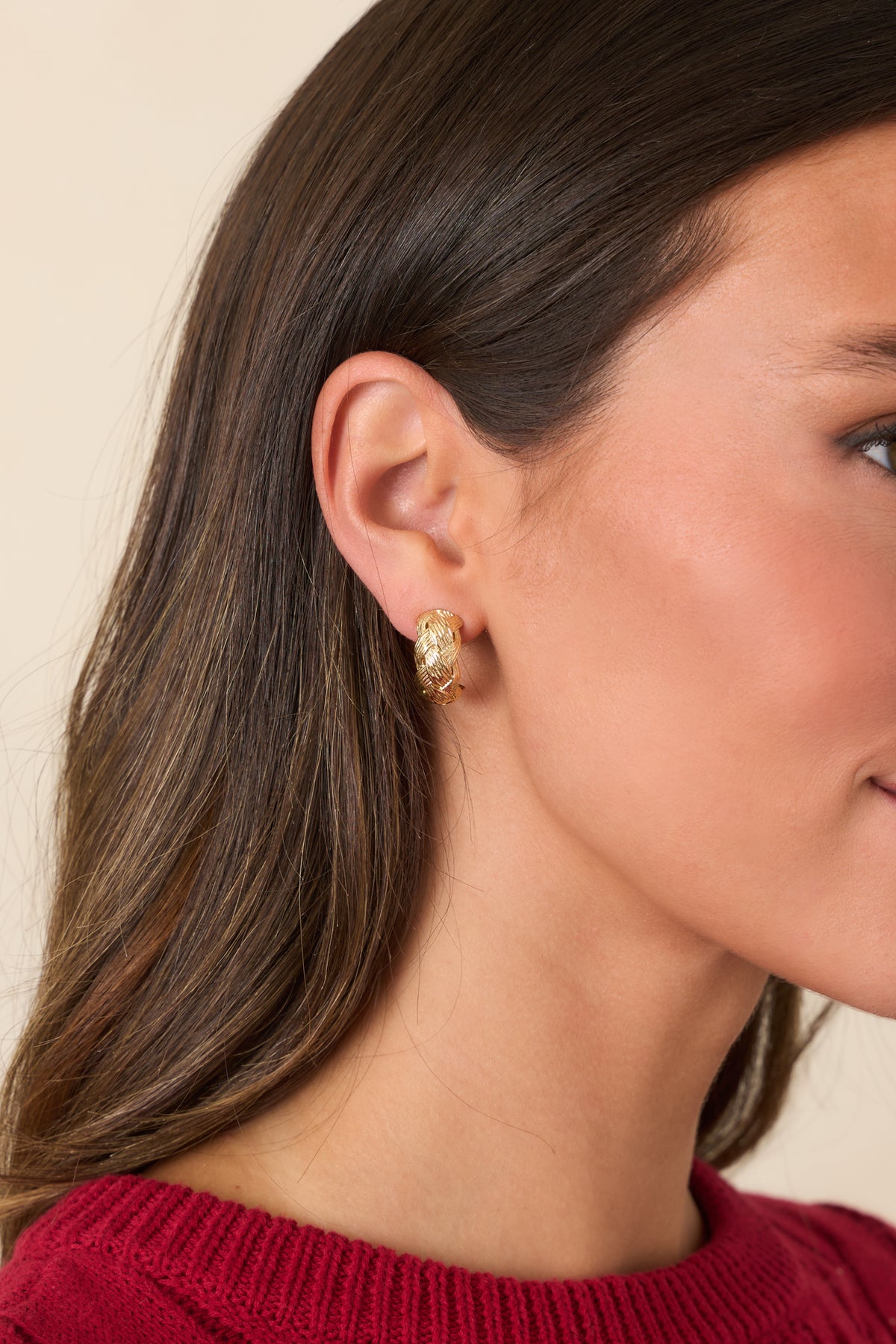 Gold-tone hoop earring featuring an intricate woven design with finely textured detailing.