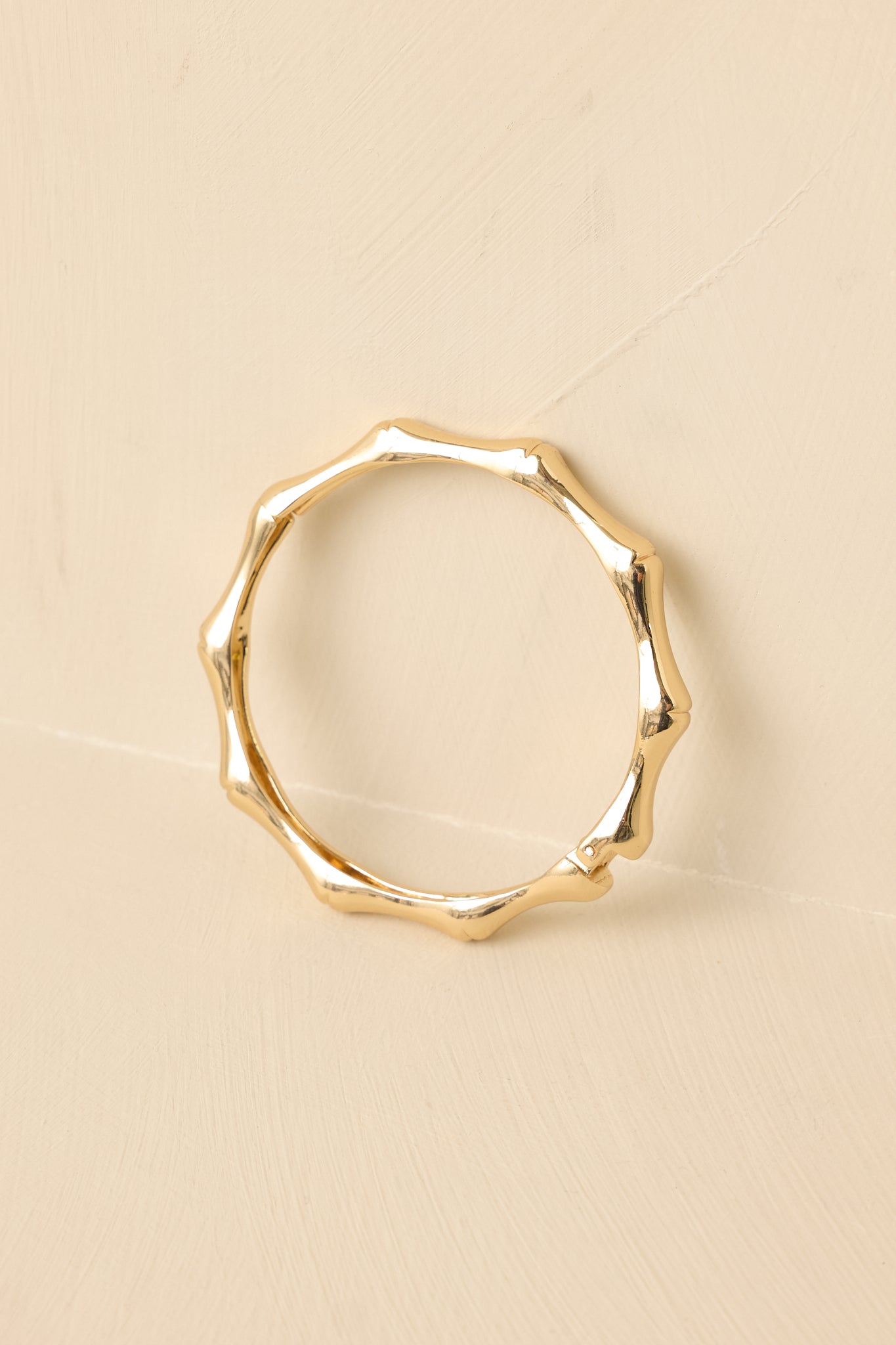Gold-tone bamboo-inspired bangle displayed against a beige background, showcasing the hinged opening and snap closure.