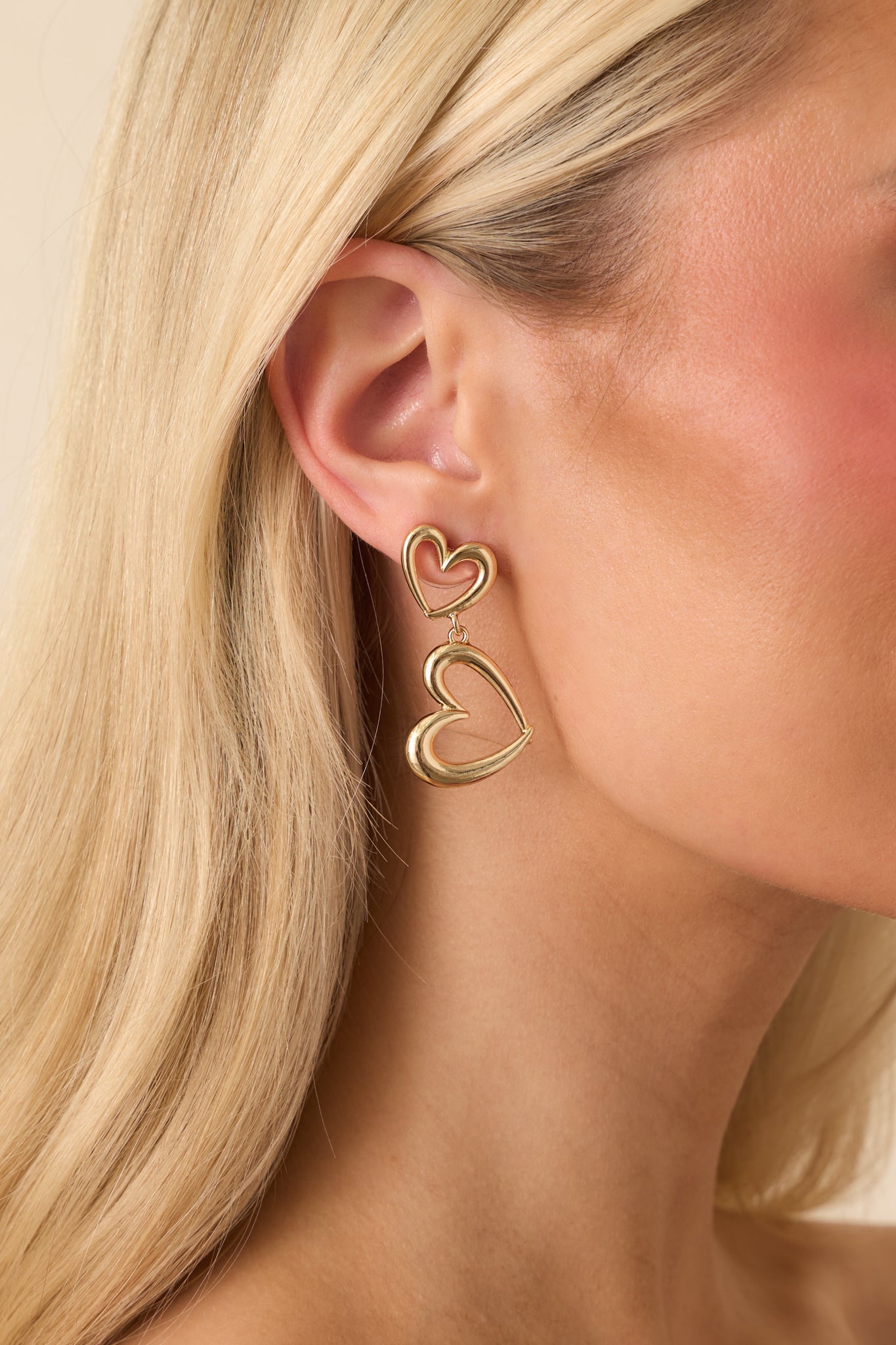 Cropped front view of the gold-tone drop earrings featuring a double open-heart design and polished finish.