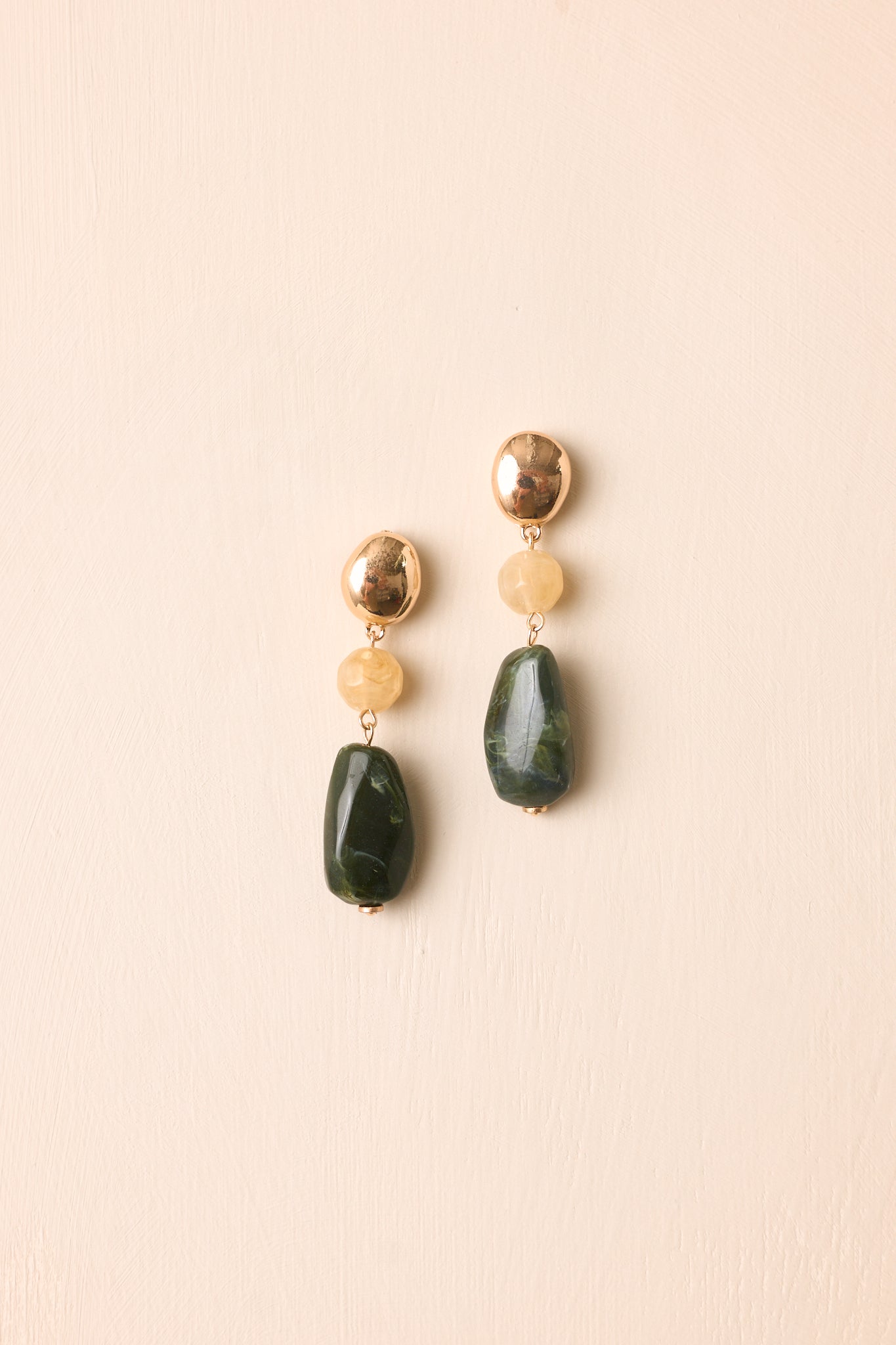 Gold-tone drop earrings displayed against a beige background, featuring faceted honey-colored beads and marbled green bead accents with an elongated silhouette.