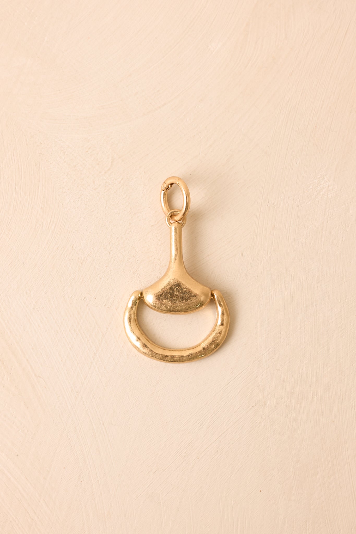 Gold-tone decorative charm featuring a sculptural horsebit silhouette with a softly textured finish and polished spring-ring attachment.