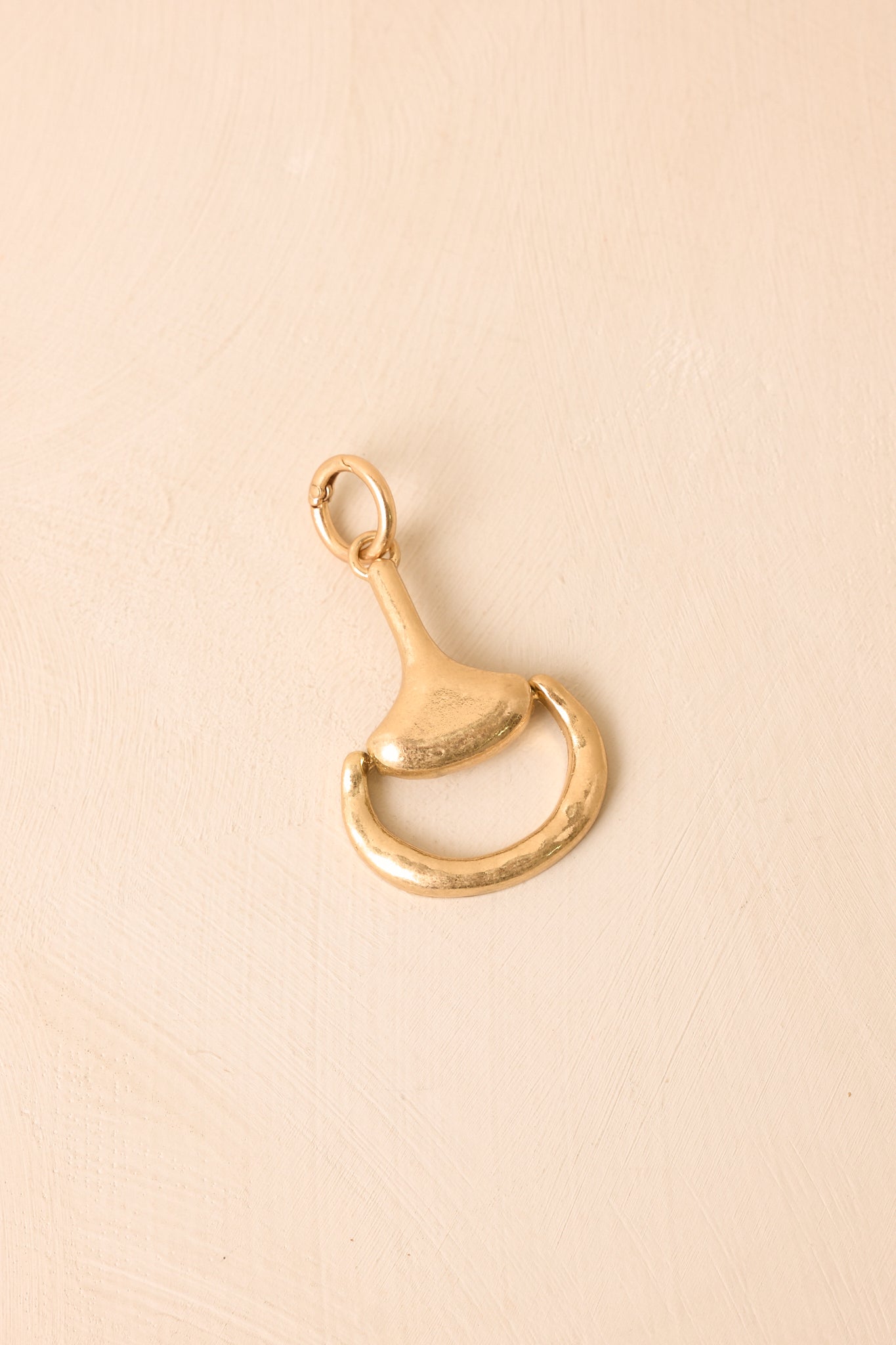 Close view of the gold-tone horsebit charm highlighting the sculptural hardware-inspired design, textured finish, and spring-ring clasp.