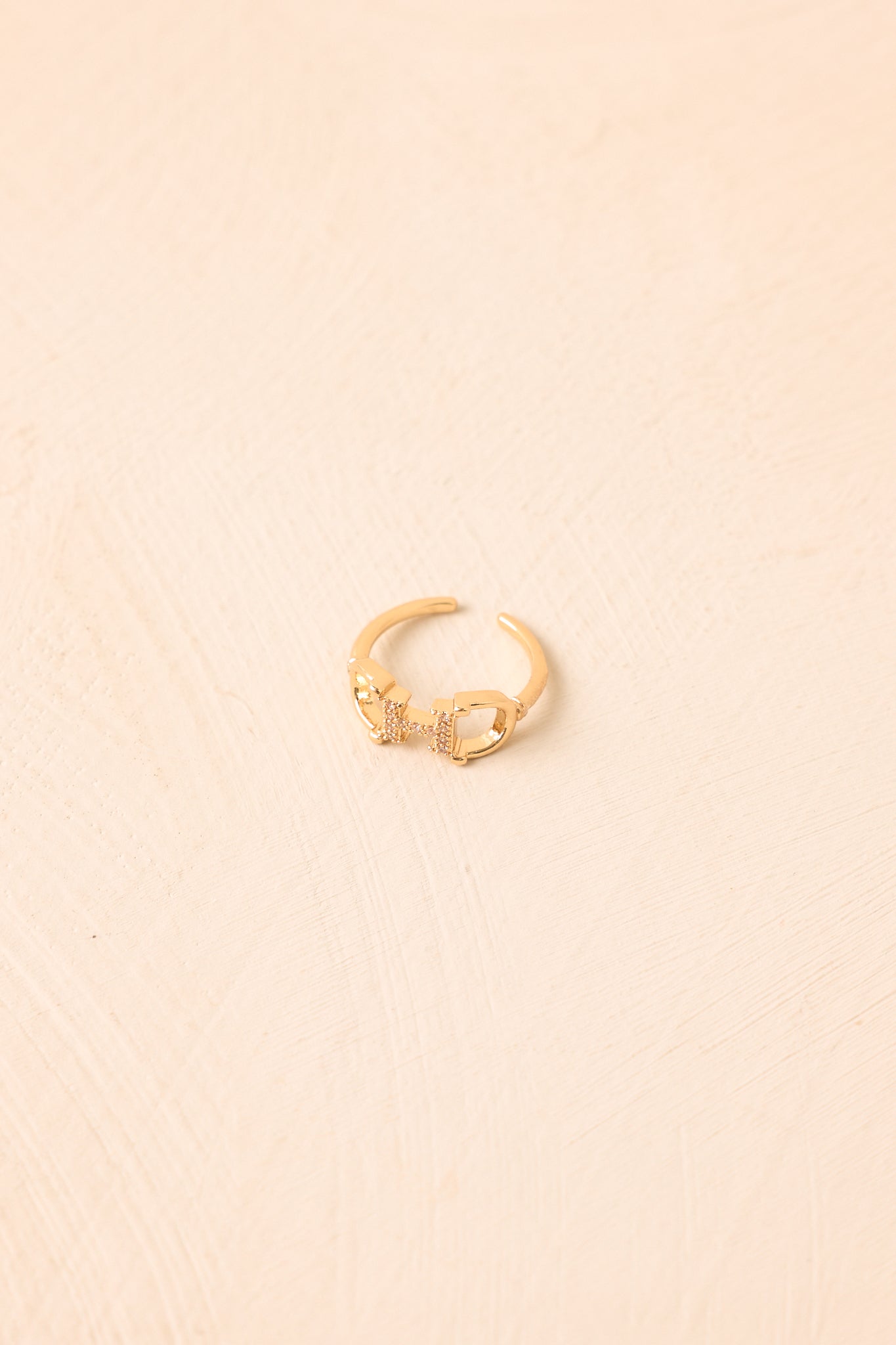 Gold-tone horsebit ring displayed against a beige background, highlighting the sculptural centerpiece, crystal accents, and adjustable open band.