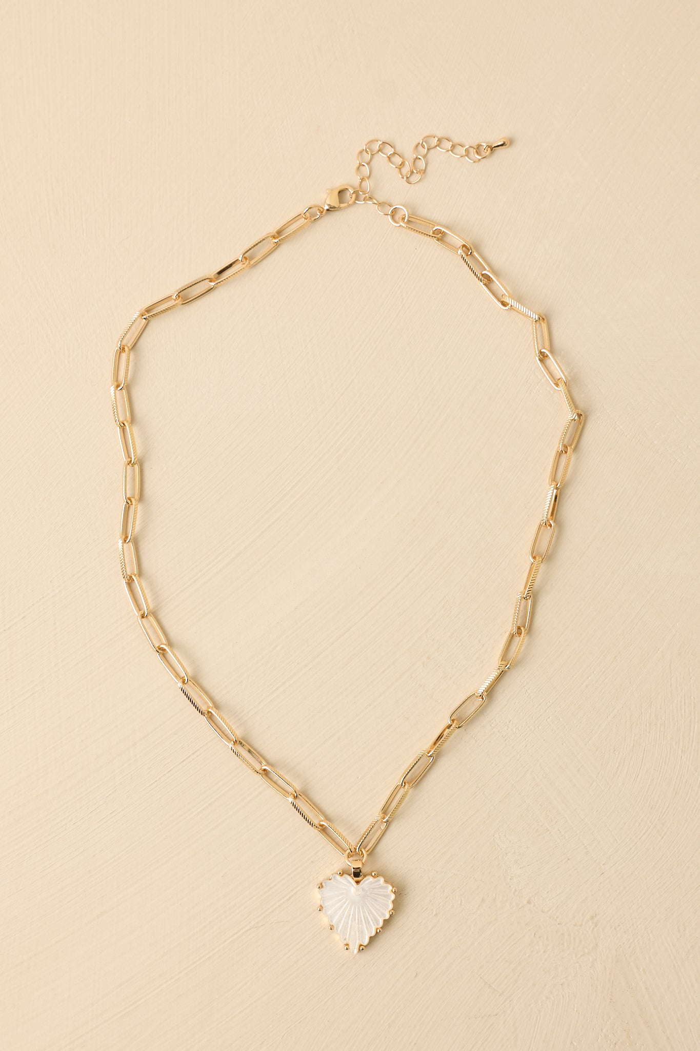 Gold-tone necklace featuring a textured scalloped heart pendant suspended from a slim paperclip-style chain.