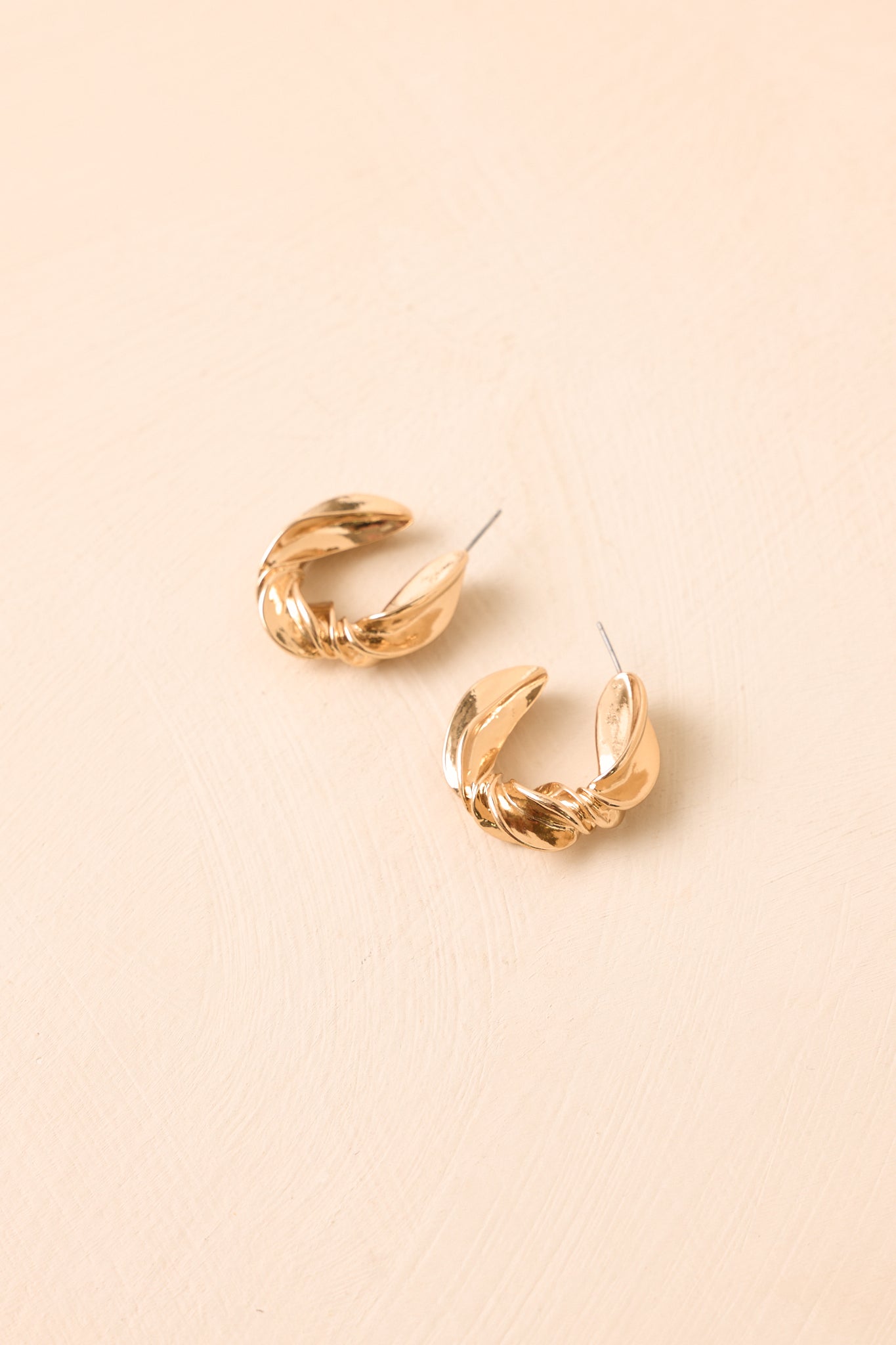 Gold twisted hoop earrings displayed against a beige background, highlighting their smooth curves and contemporary silhouette.