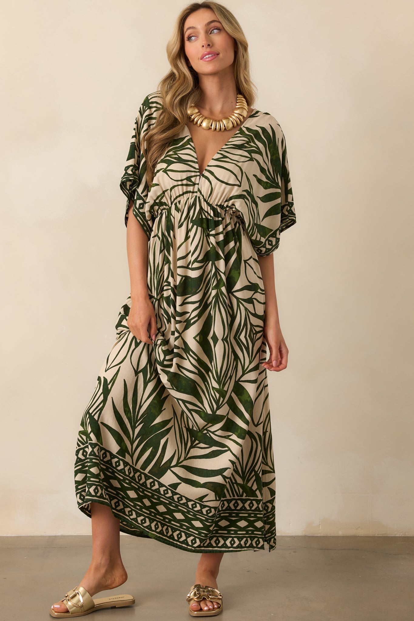 Green and beige palm leaf print maxi dress shown from the front, emphasizing the open V-back, elastic waist, and the geometric detailing along the skirt.