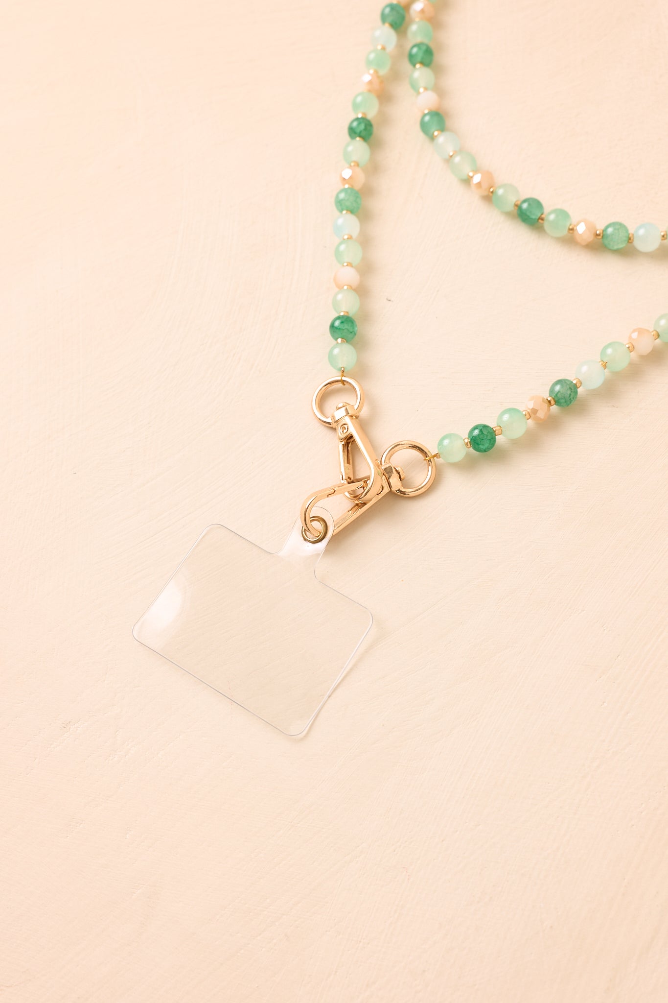 Detailed view of the green beaded phone lanyard, highlighting the smooth bead texture, coordinating colors, gold spacers, and clasp detail.