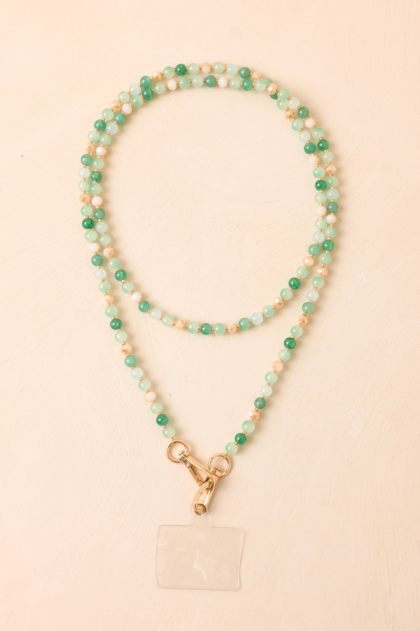 Green beaded phone lanyard displayed against a beige background, highlighting the polished beads and jewelry-inspired design.