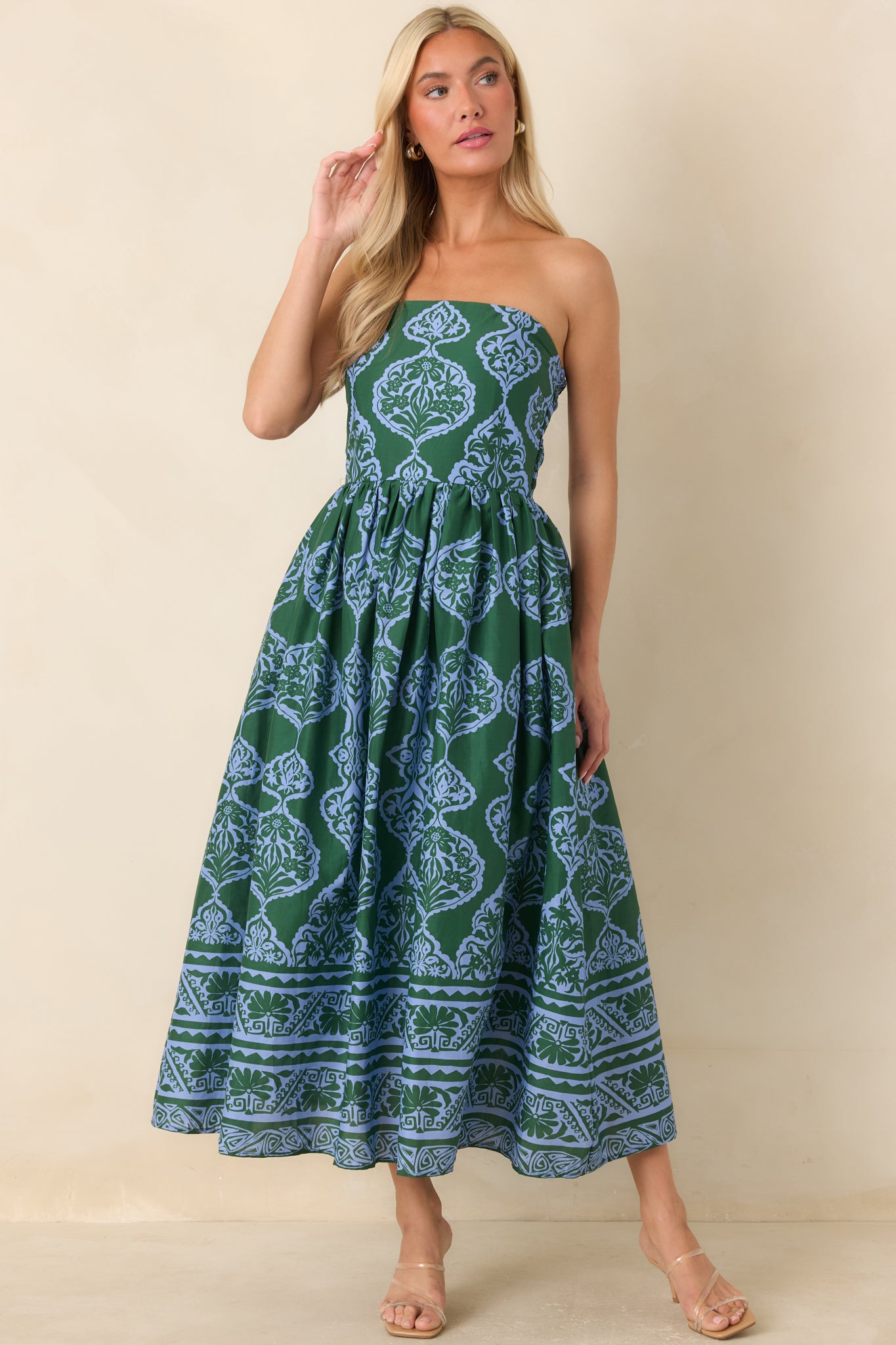 A woman modeling a strapless midi dress with a green and blue paisley block print pattern, standing against a solid beige background.