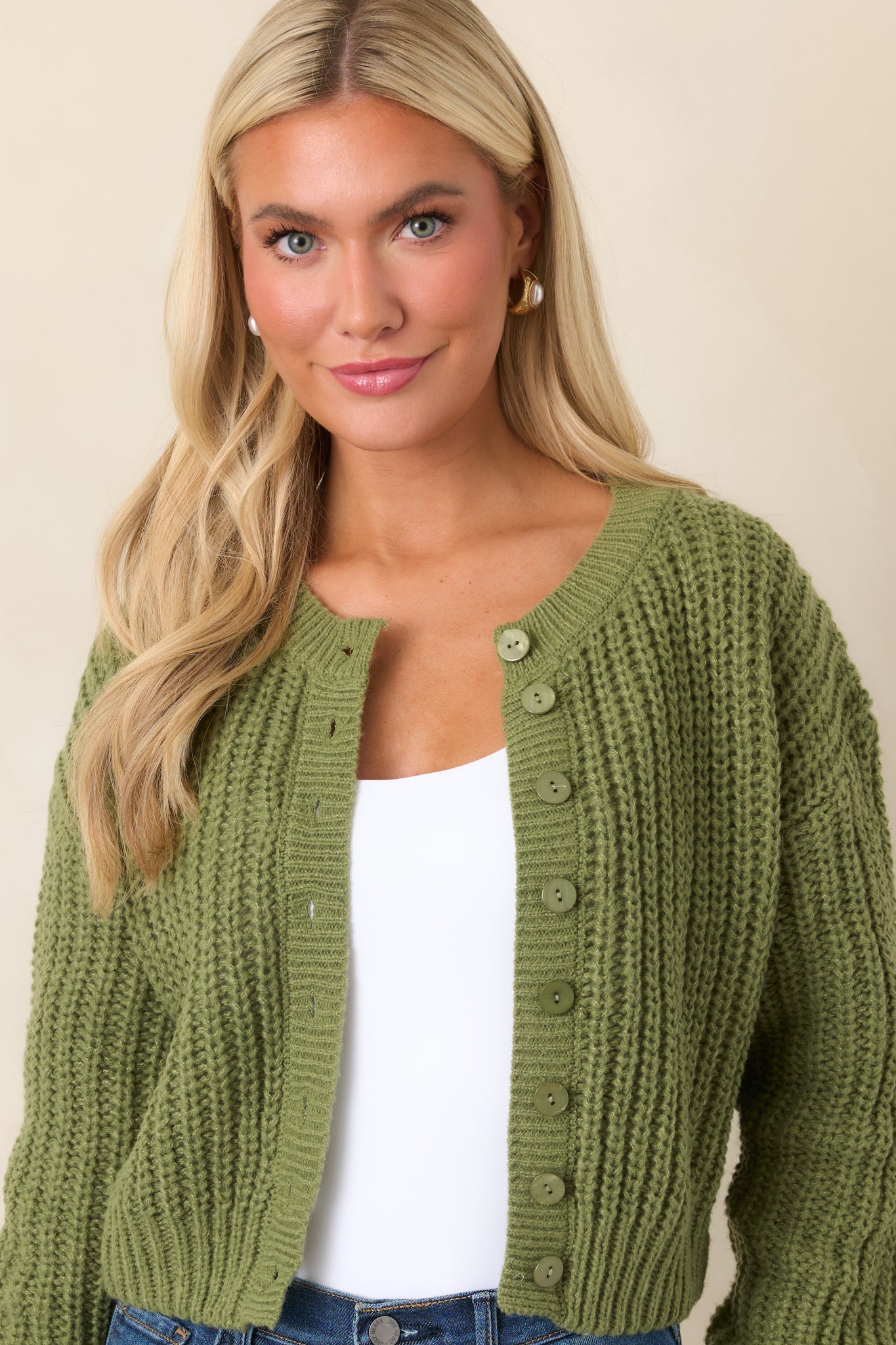 Green cropped cardigan highlighting the raised cable-inspired stitching across the bodice and softly ribbed sleeve cuff.