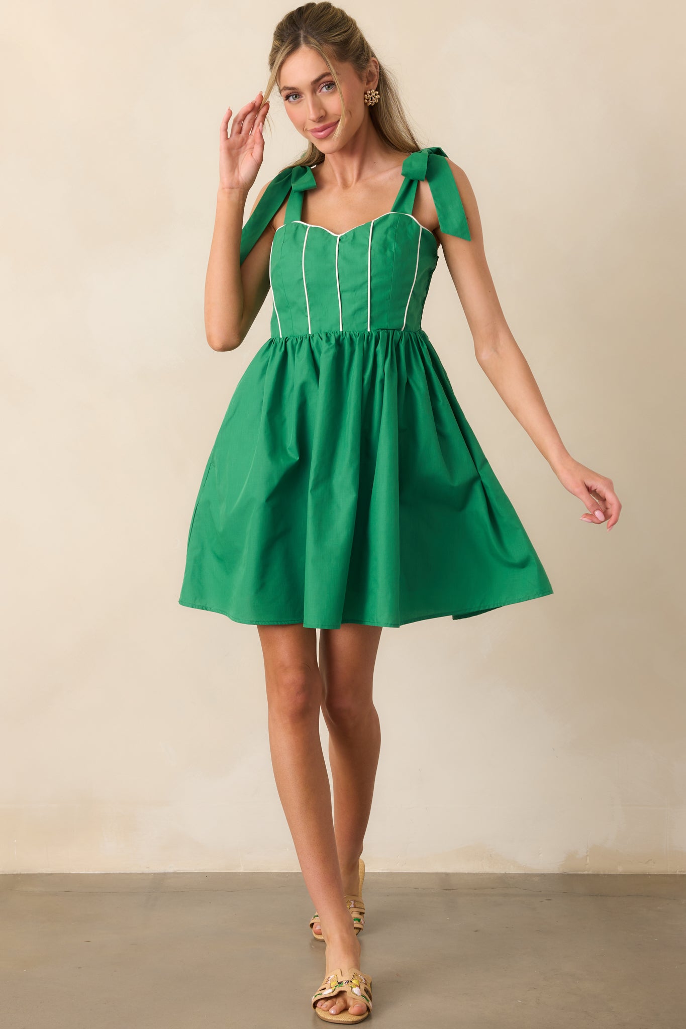 Green mini dress with sweetheart neckline and white corset-style trim, shown with bow-tied shoulder straps and flared skirt.