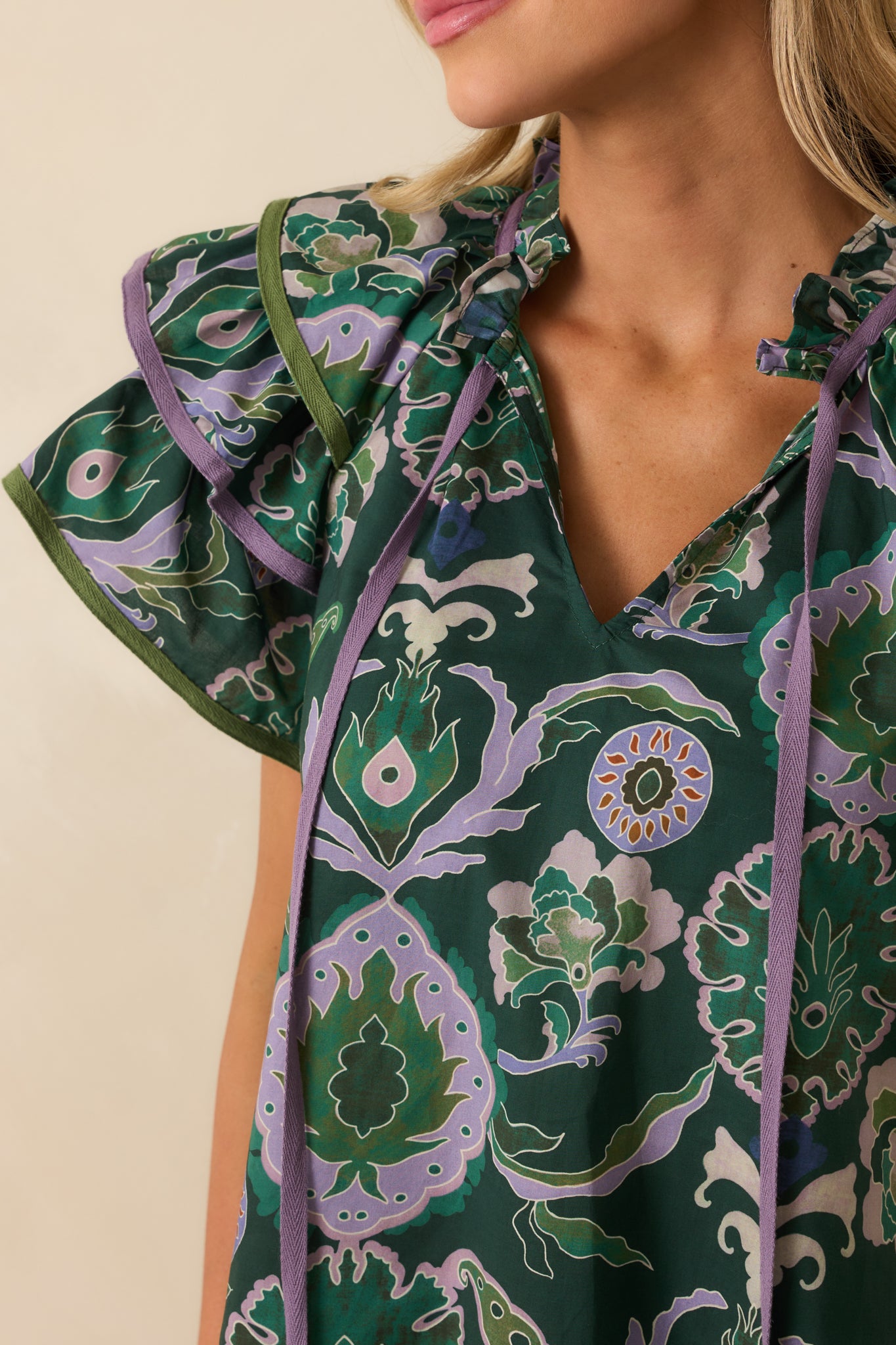 Detailed view of green fabric with multicolor print, ruffle-trimmed v-neckline, and self-tie tassel accents.